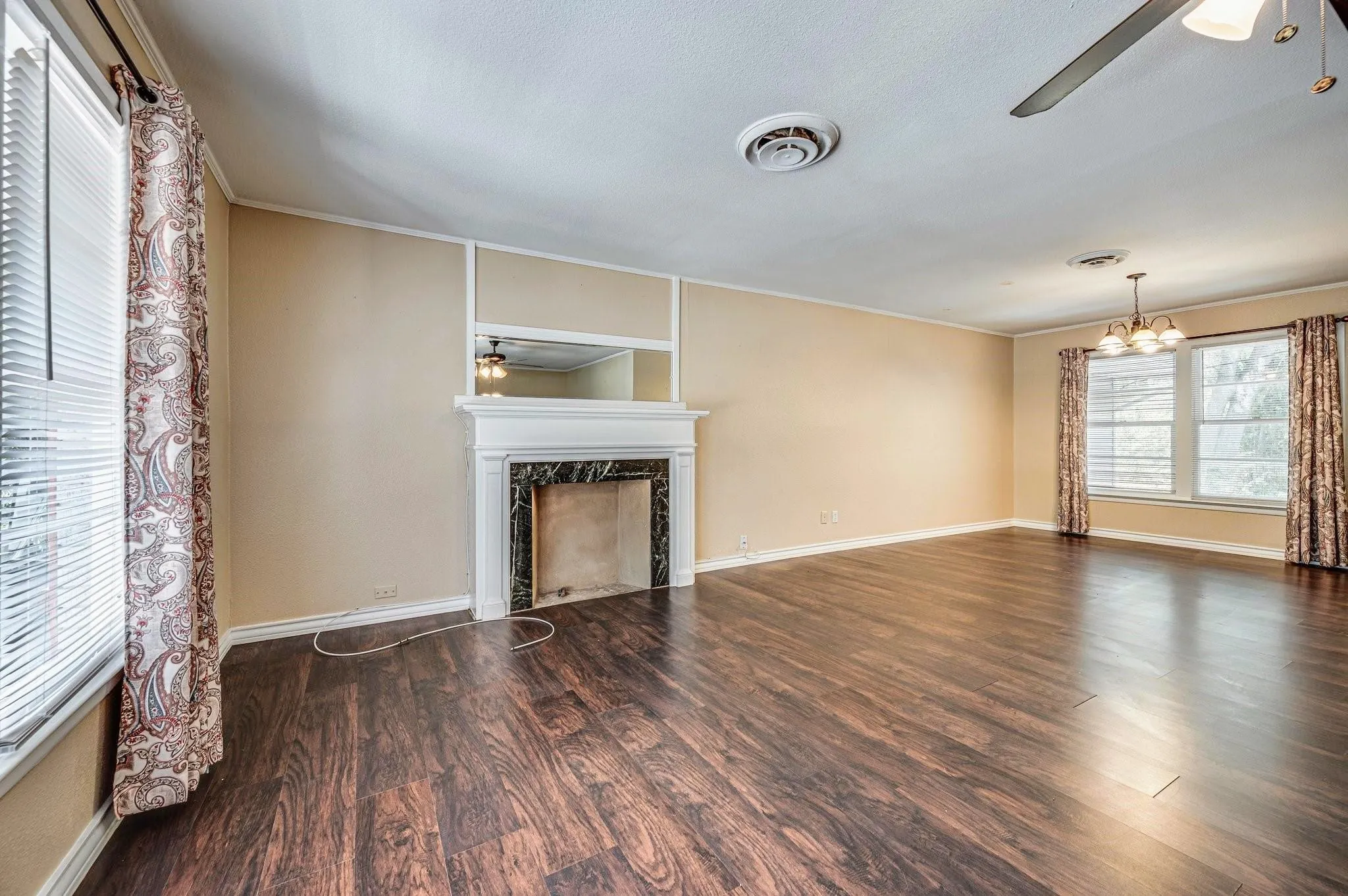 Spacious room featuring rich wood-finish flooring, a decorative fireplace with a marble-look surround, and multiple windows for abundant light