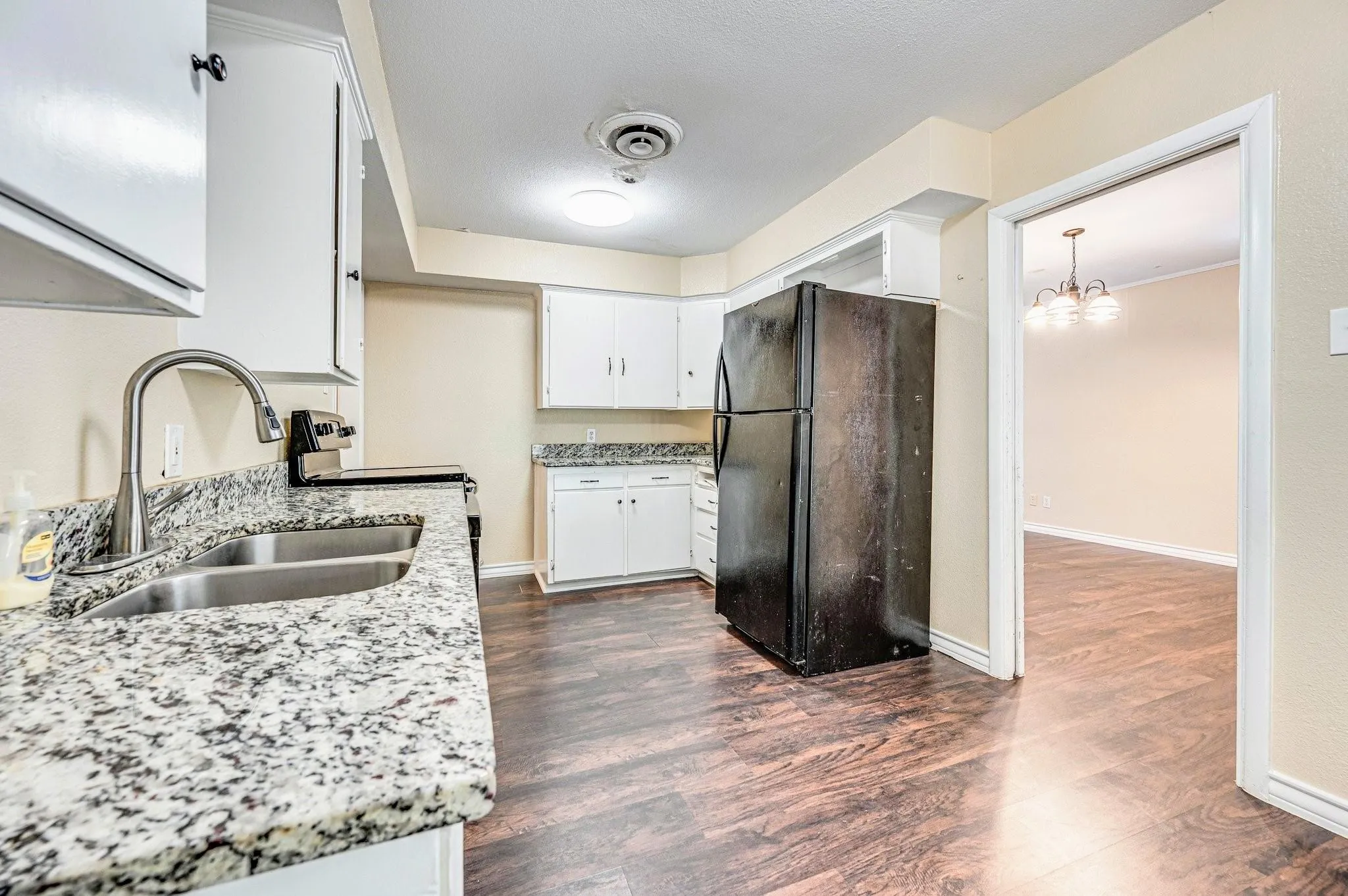 Kitchen featuring white cabinetry, speckled countertops, stainless steel double basin sink with gooseneck faucet, and dark wood-finish flooring