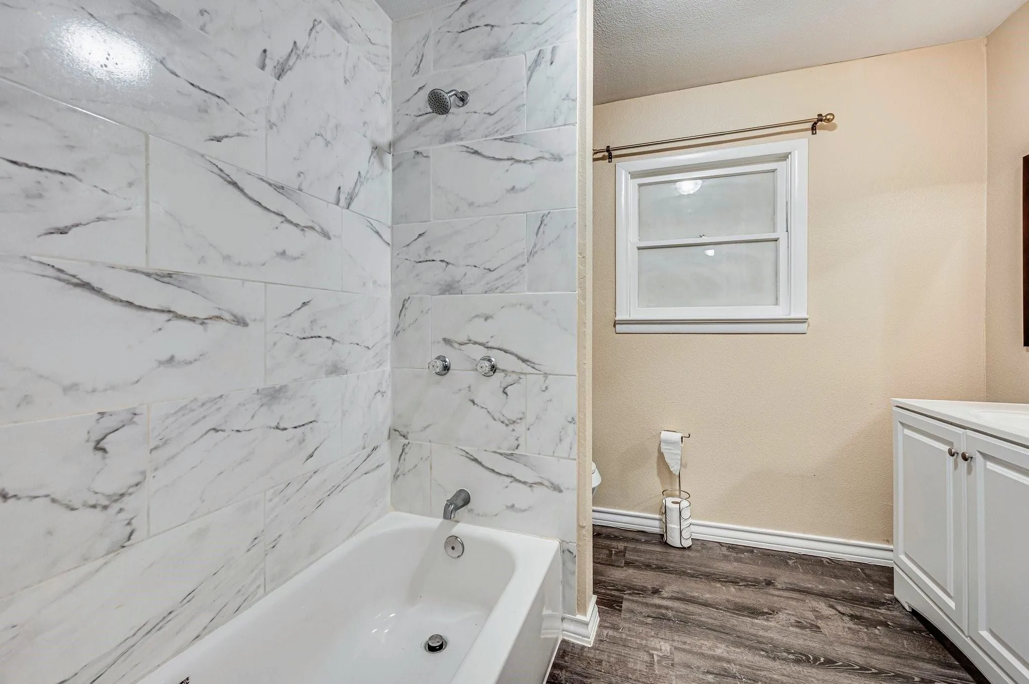 Full bathroom featuring a white porcelain bathtub with chrome fixtures, surrounded by large format white tile with gray veining