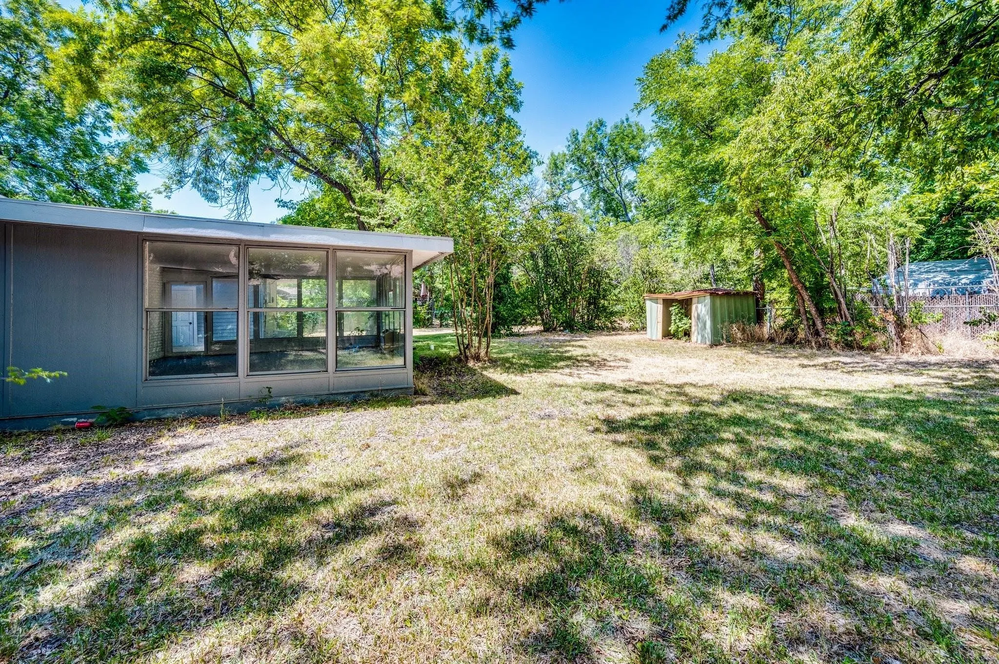 Expansive backyard featuring a sunroom addition with large windows and an outdoor storage structure