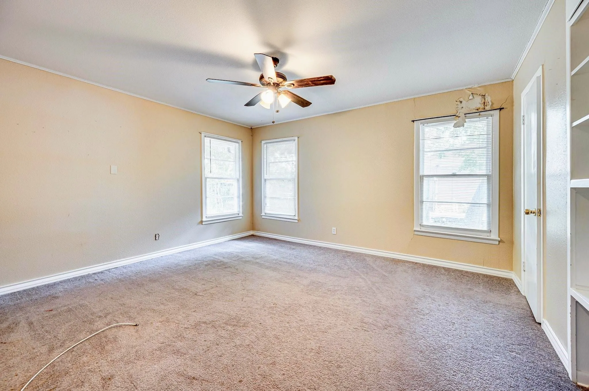 Spacious room featuring neutral wall tones, three windows for natural light, a ceiling fan, and built-in shelving