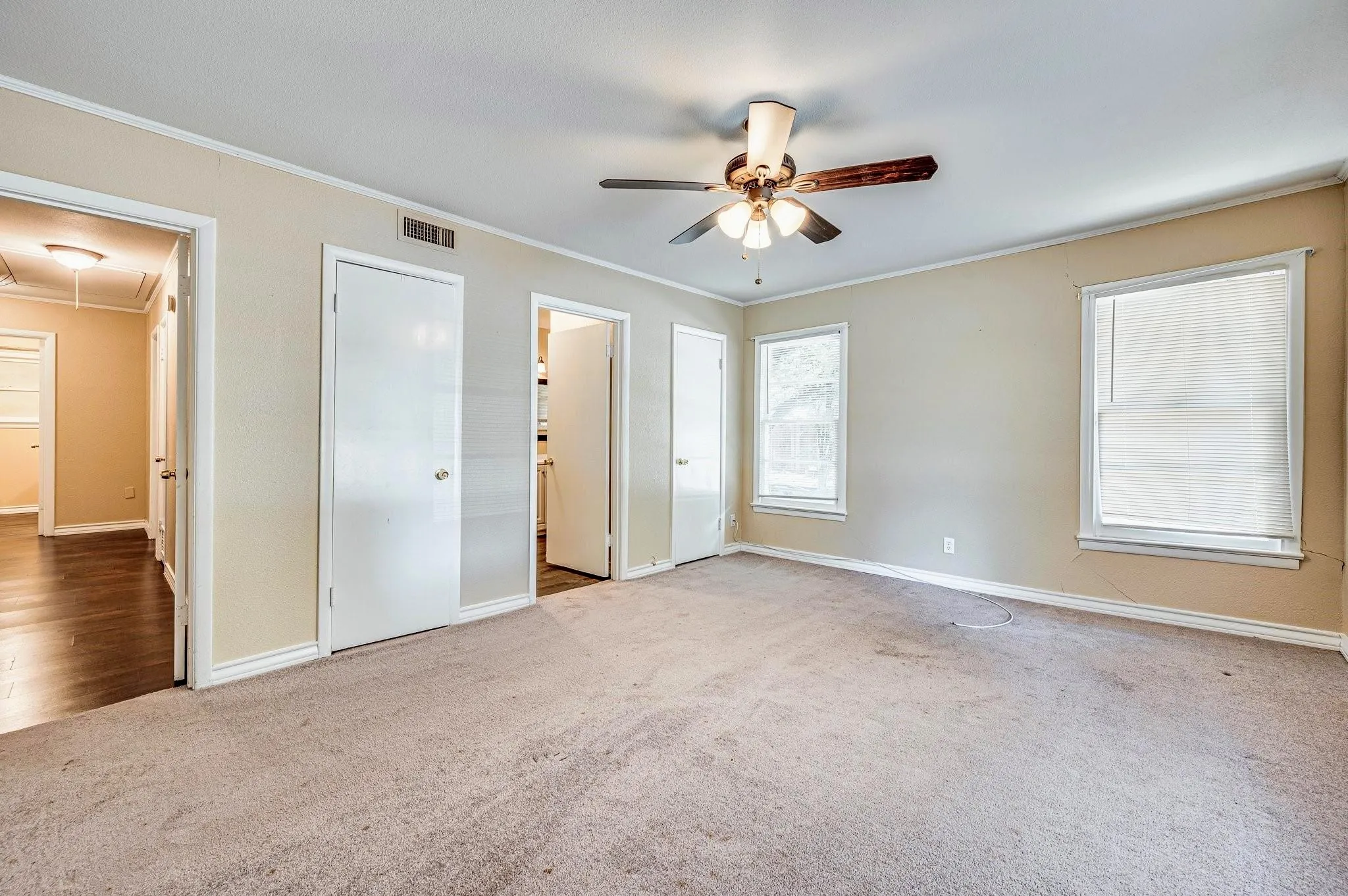 Carpeted room featuring a ceiling fan with light fixture, two windows with blinds, and multiple doorways providing access to other areas of the property