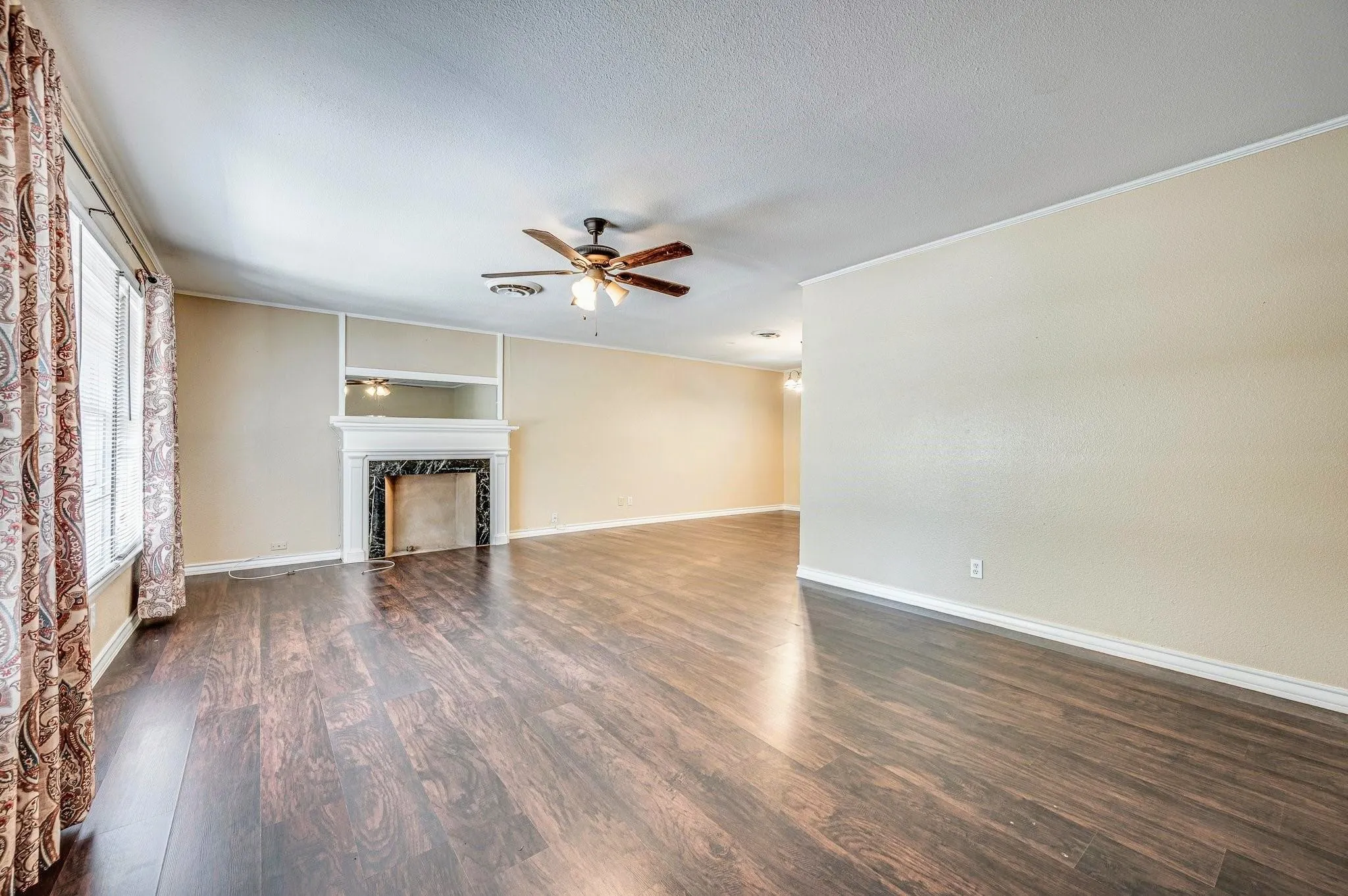 Spacious living area featuring dark wood-finish flooring, a fireplace with a white mantel and dark stone surround, and light-toned walls