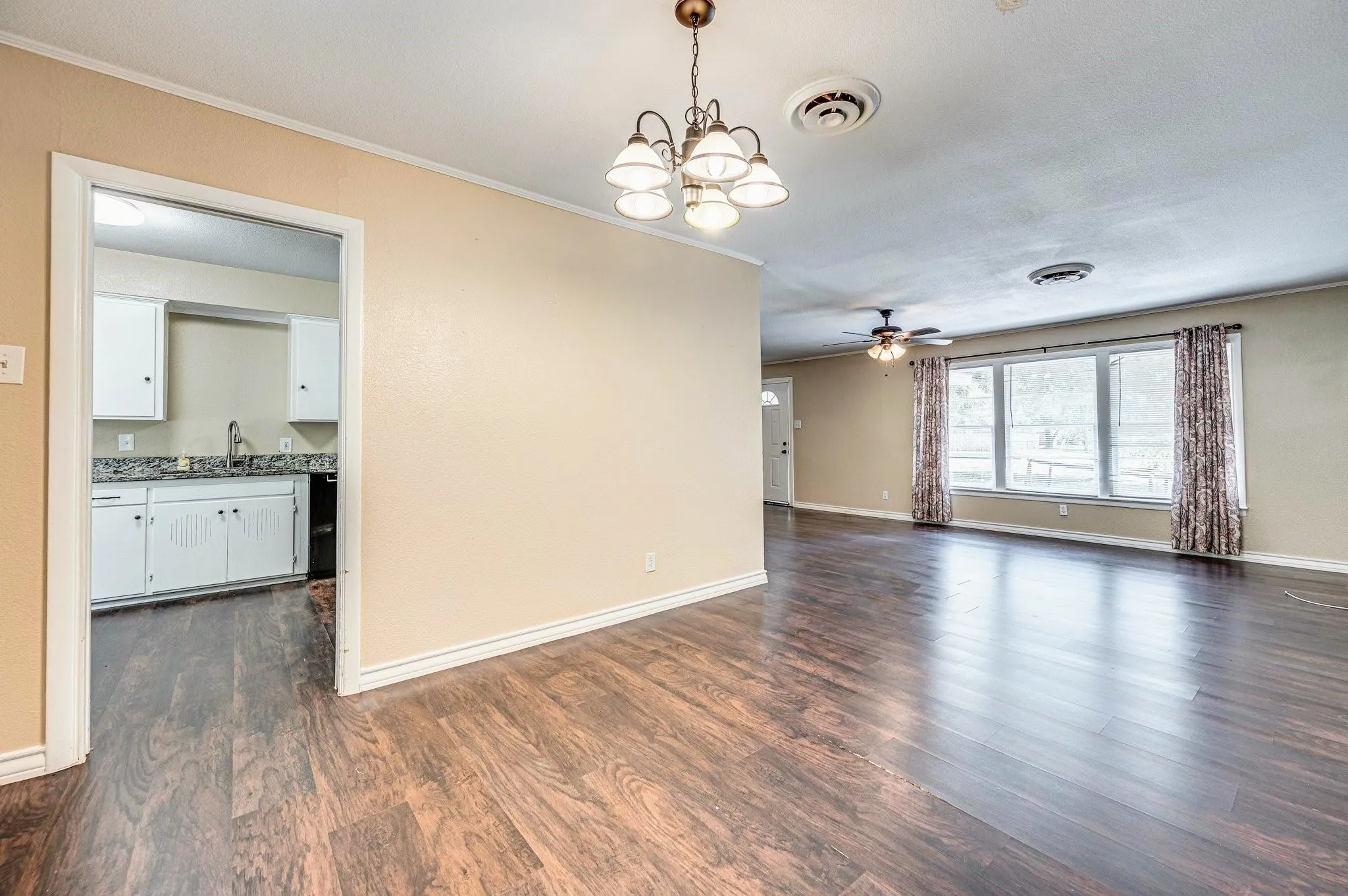Spacious interior featuring wood-finish flooring, a contemporary chandelier, and a bright window with patterned drapes