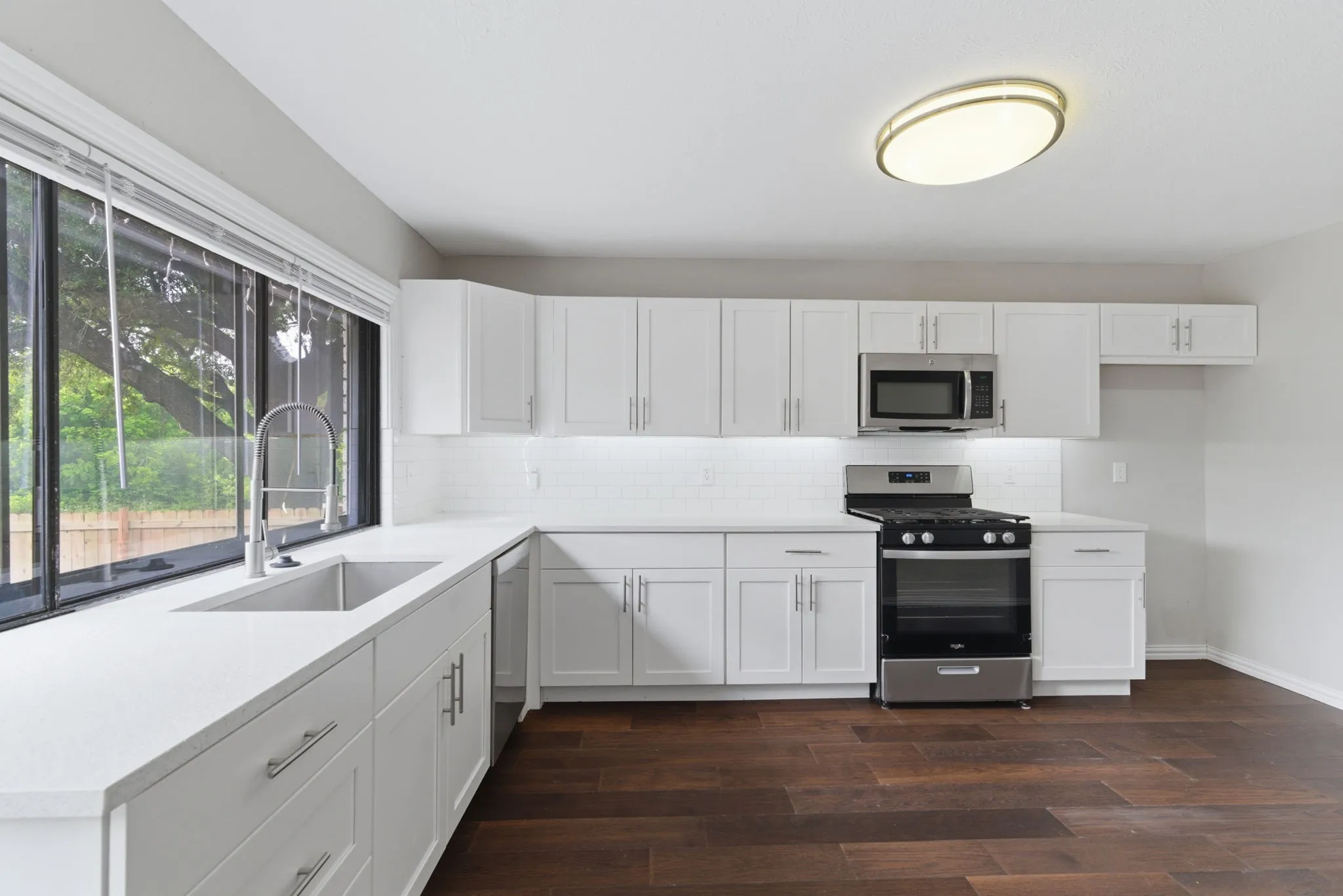 Contemporary kitchen with white cabinetry, stainless steel appliances, a deep basin sink, and wood-finish flooring