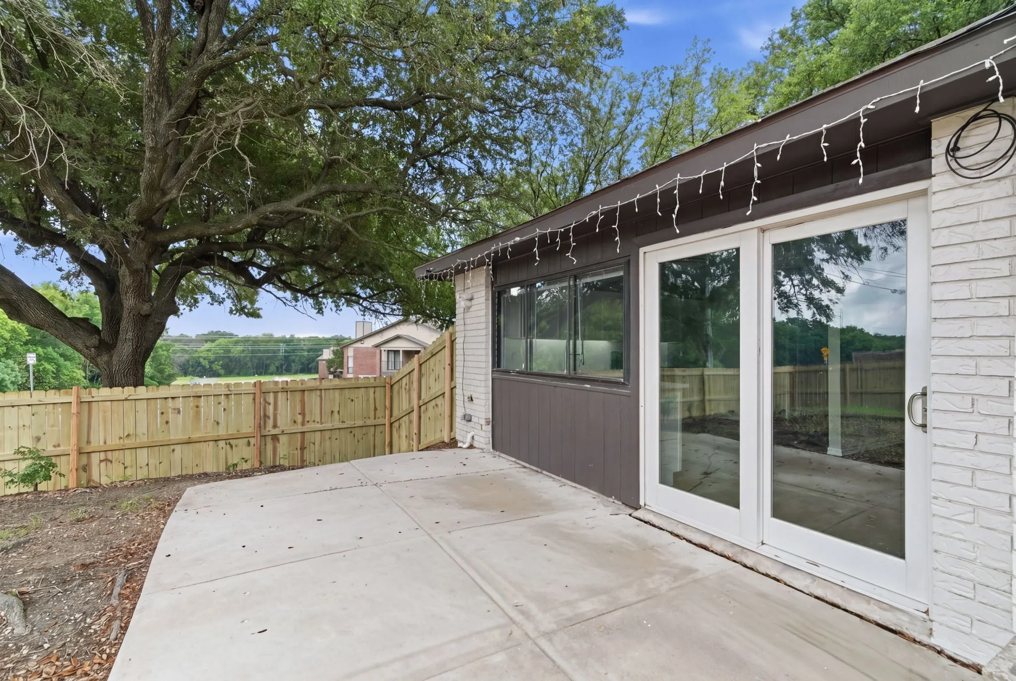 Spacious rear patio featuring concrete paving, a new wood privacy fence, and a mature tree