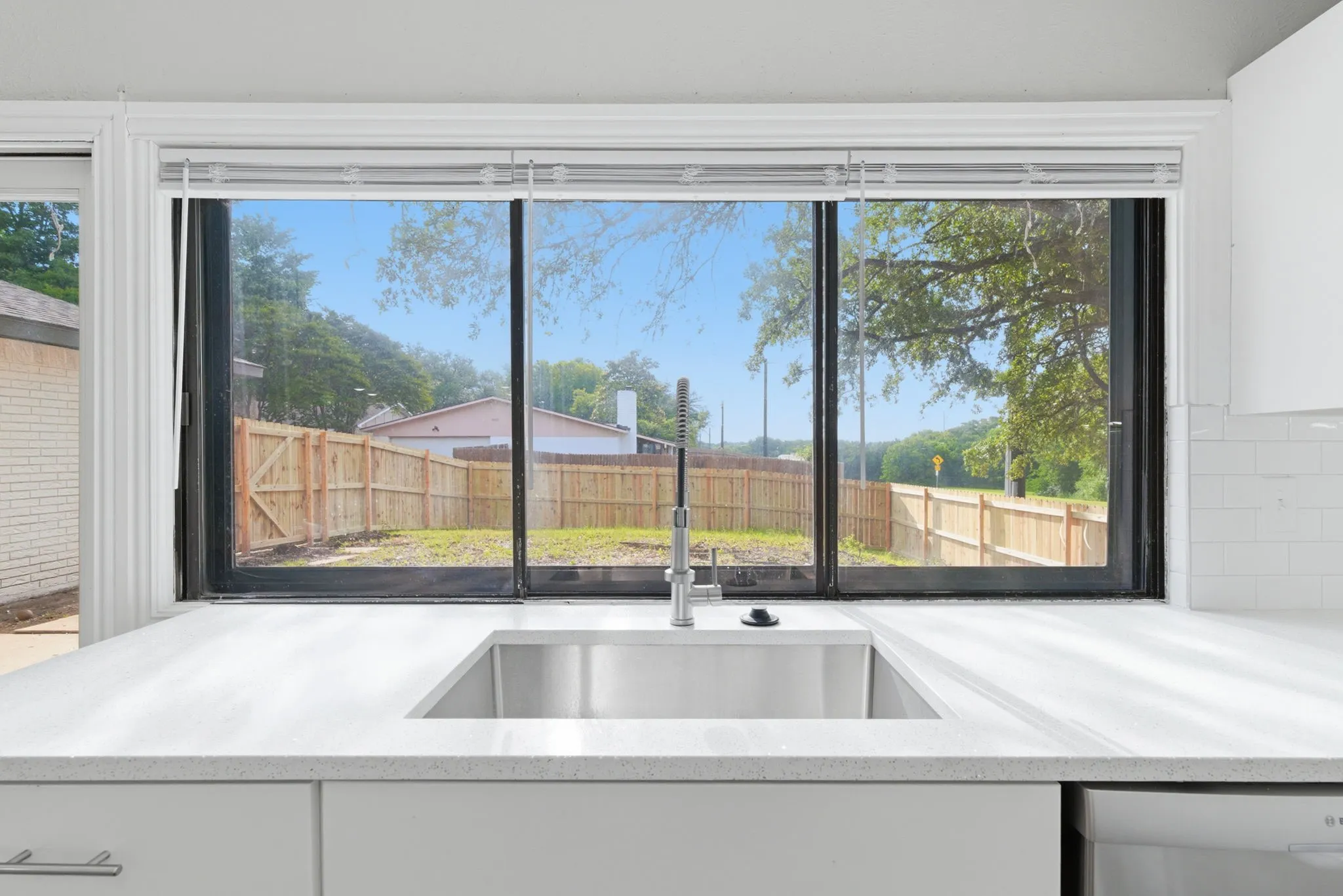 Kitchen featuring a stainless steel undermount sink with a gooseneck faucet, light-toned countertops, and a white subway tile backsplash