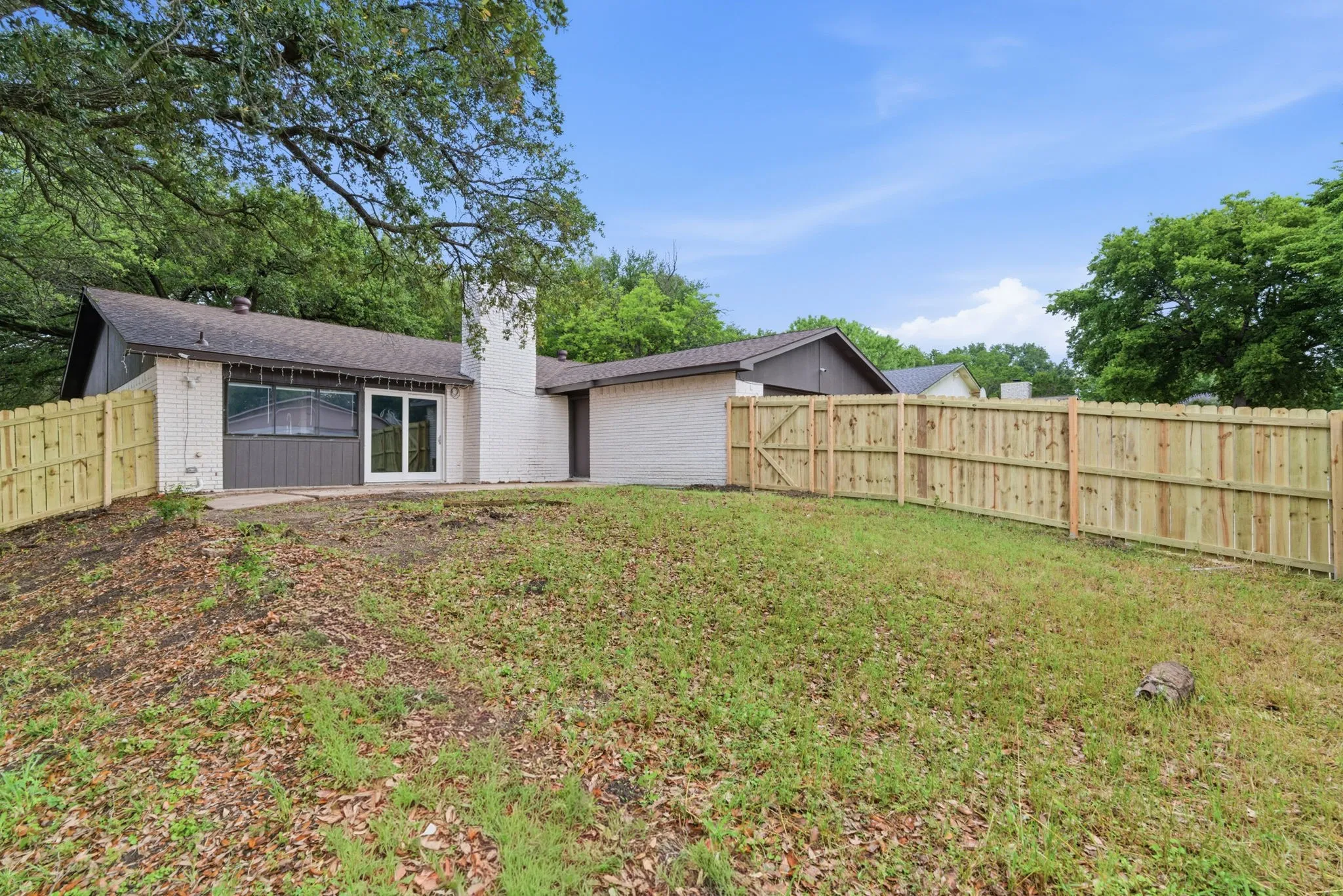 Rear exterior featuring a patio with sliding glass doors, white brick facade, and a new privacy fence