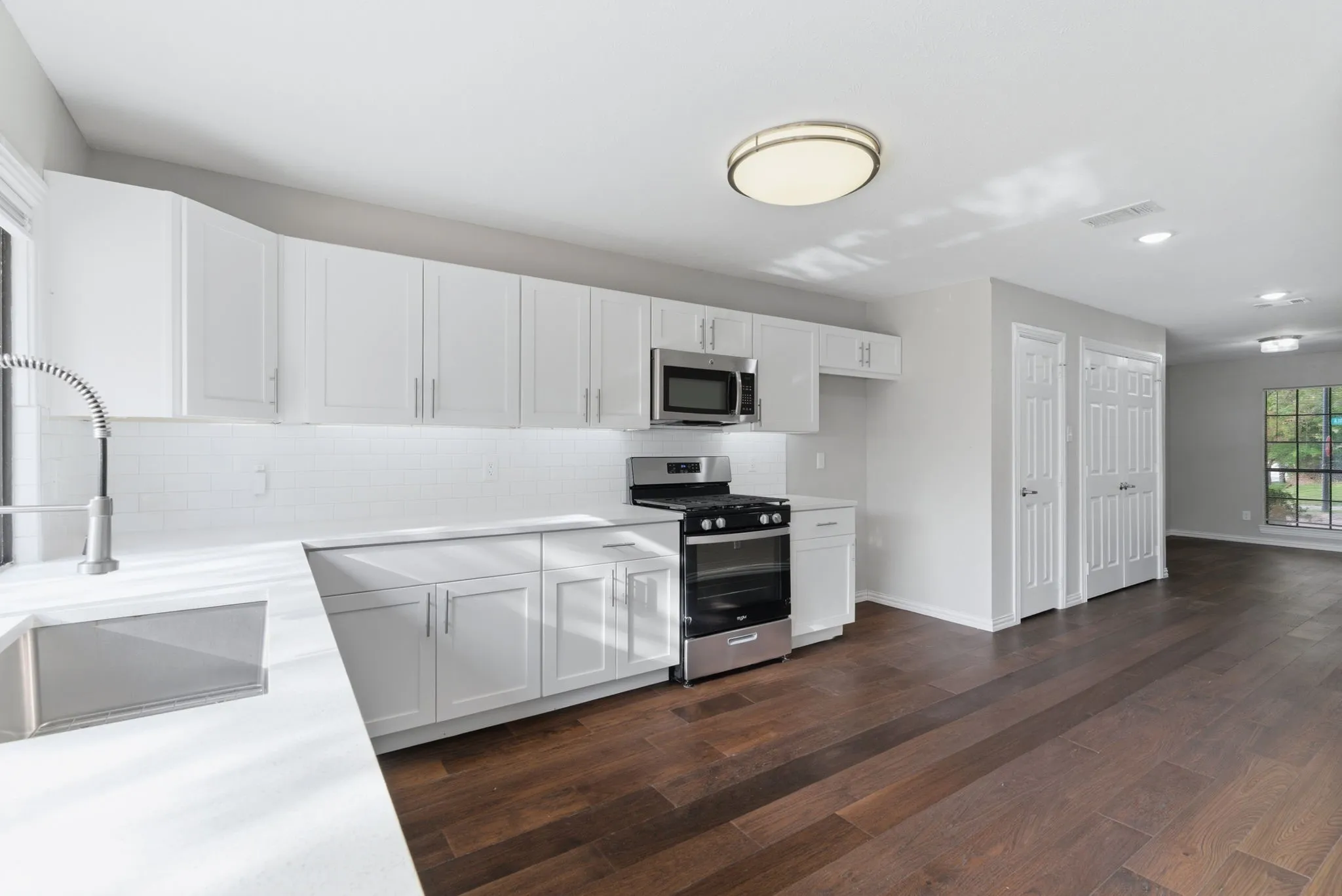 Kitchen featuring white cabinetry, stainless steel appliances, a subway tile backsplash, solid surface countertops, and wood-finish flooring