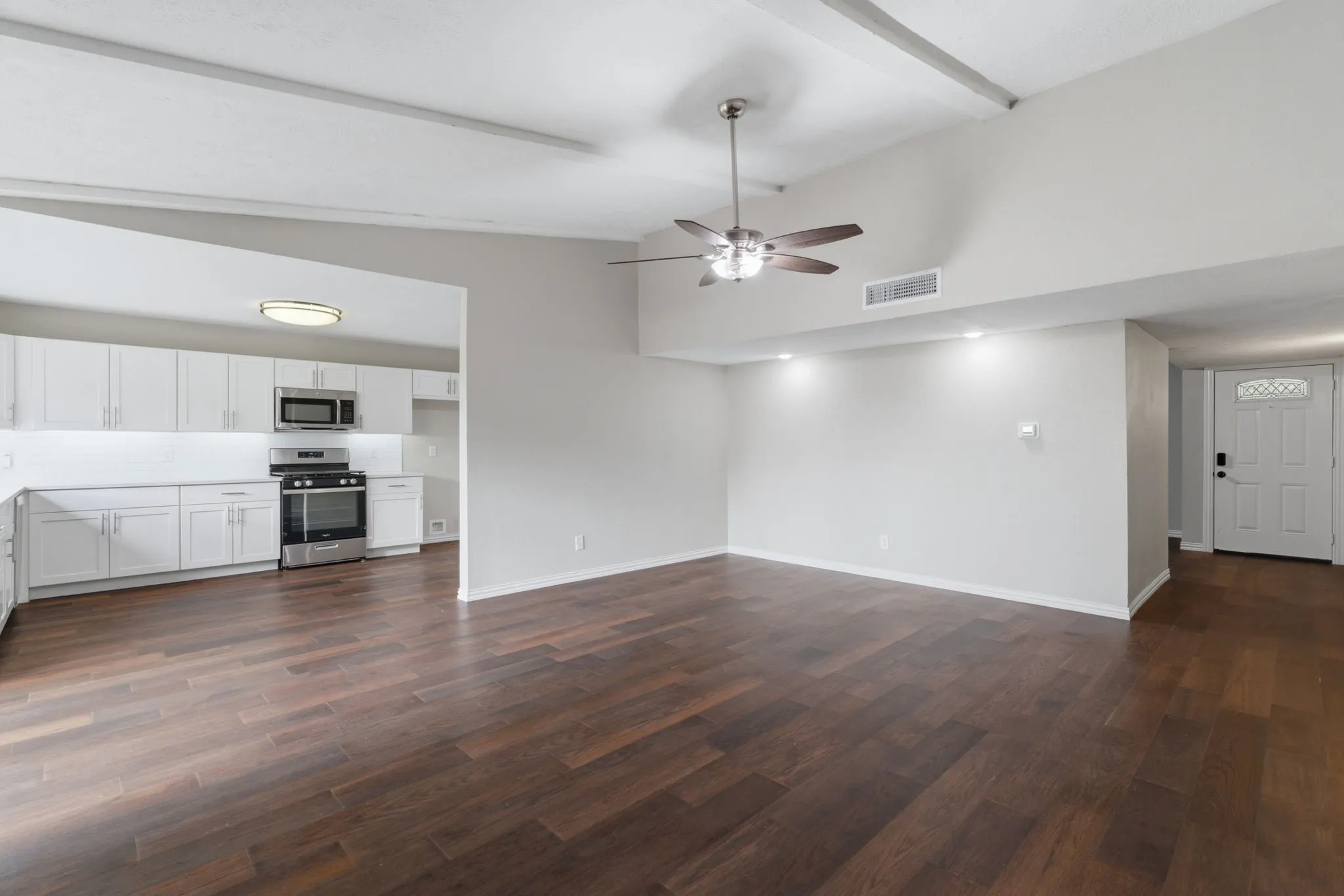 Open-concept living space featuring wood-finish flooring, a ceiling fan, recessed lighting, and a kitchen with white cabinetry and stainless steel appliances