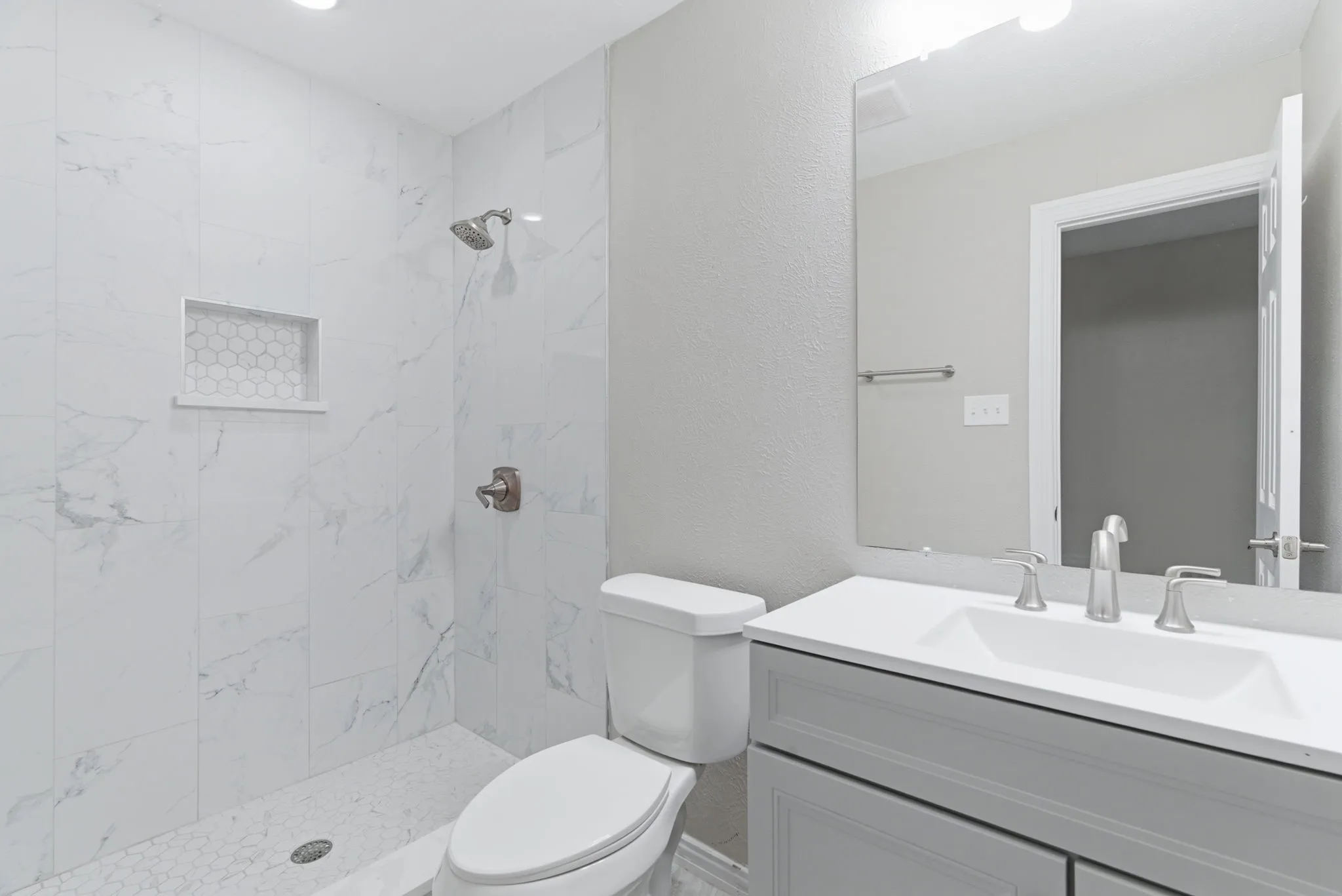 Bathroom featuring a shower with large format white marble-patterned tile, a built-in shower niche with honeycomb tile, a shower head, and a separate shower control