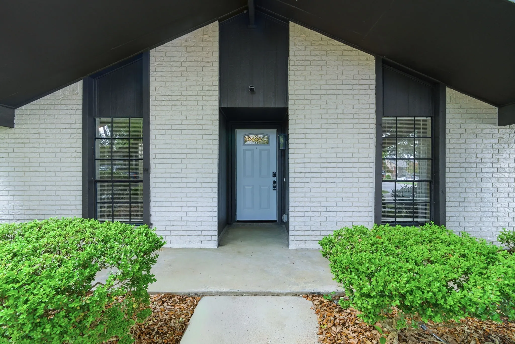 Crisp white brick exterior with a light blue entry door, accented by dark trim and an angled roofline