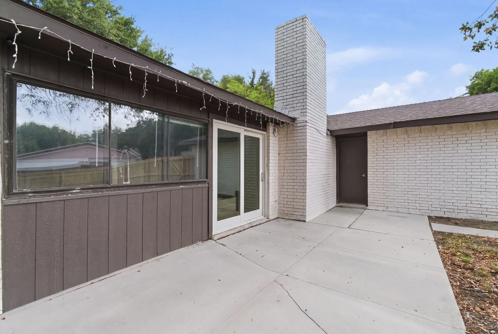 Expansive concrete patio area featuring a white brick chimney and white brick exterior walls