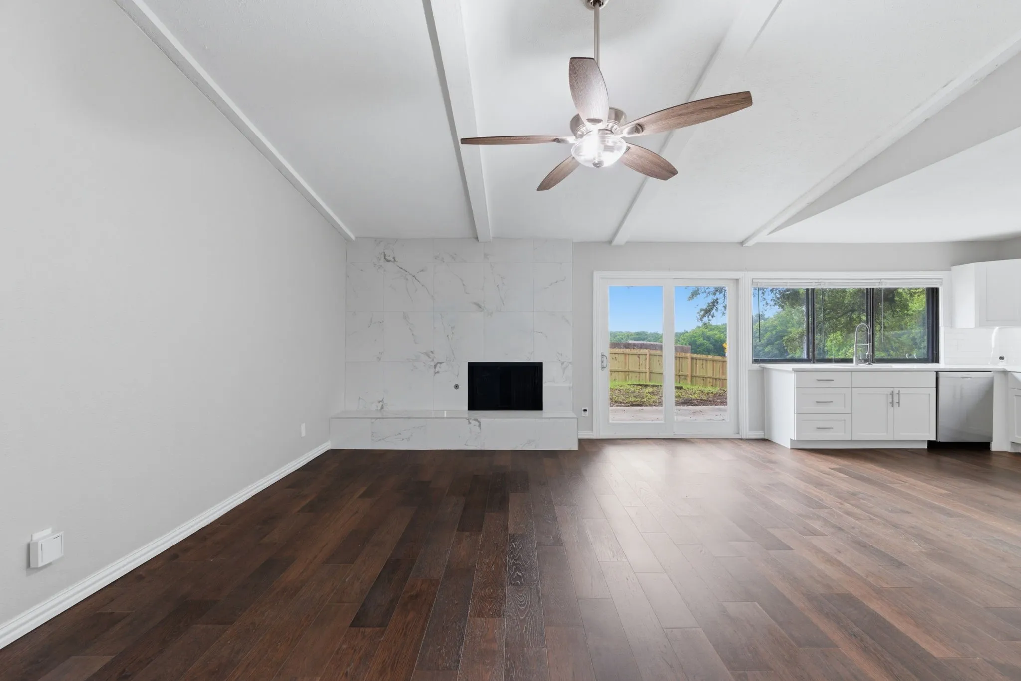 Spacious interior featuring wood-finish flooring, vaulted ceilings with exposed beams, and a modern ceiling fan