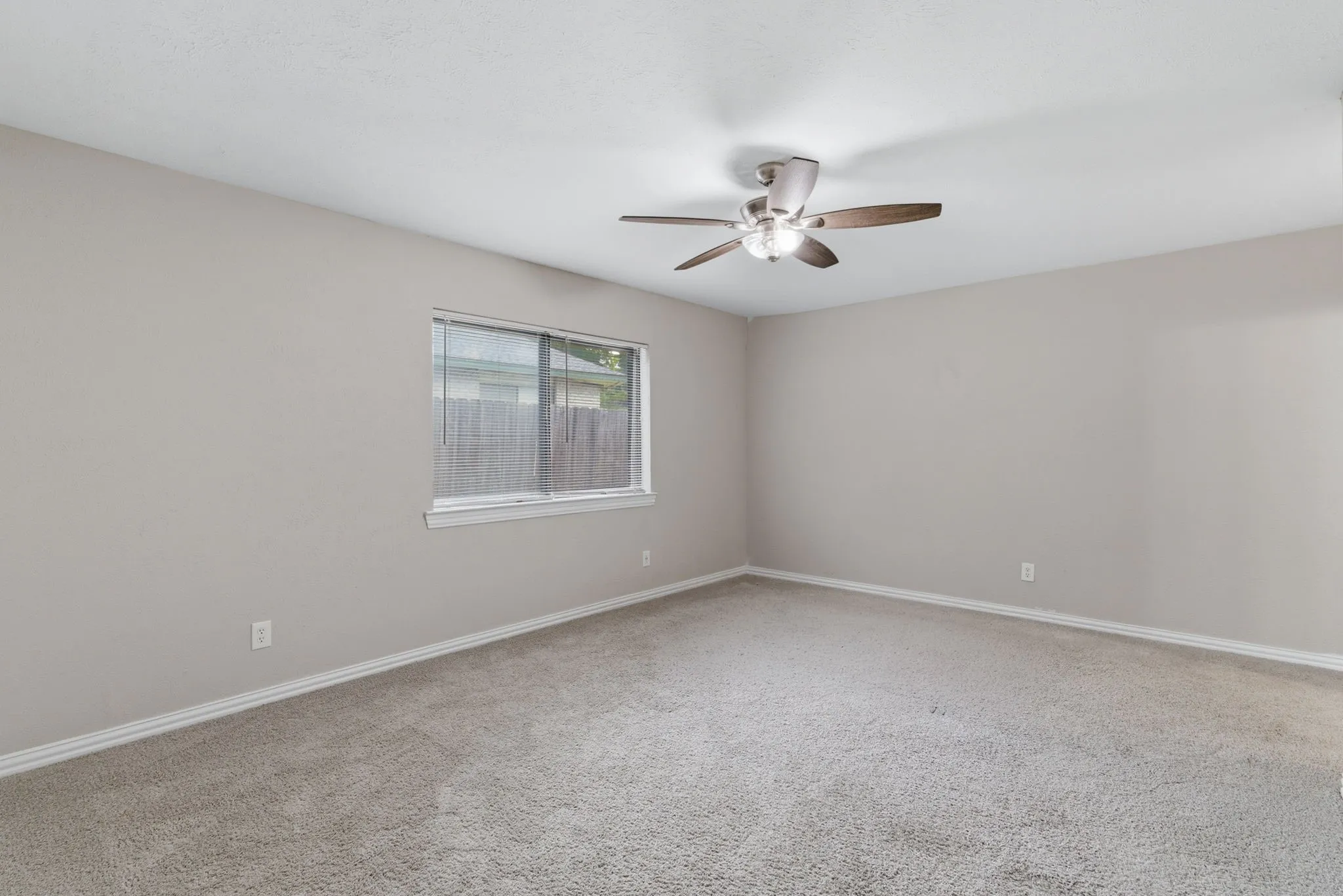 Spacious room featuring neutral paint, light gray carpeting, a multi-speed ceiling fan with lighting, a window, and white baseboards