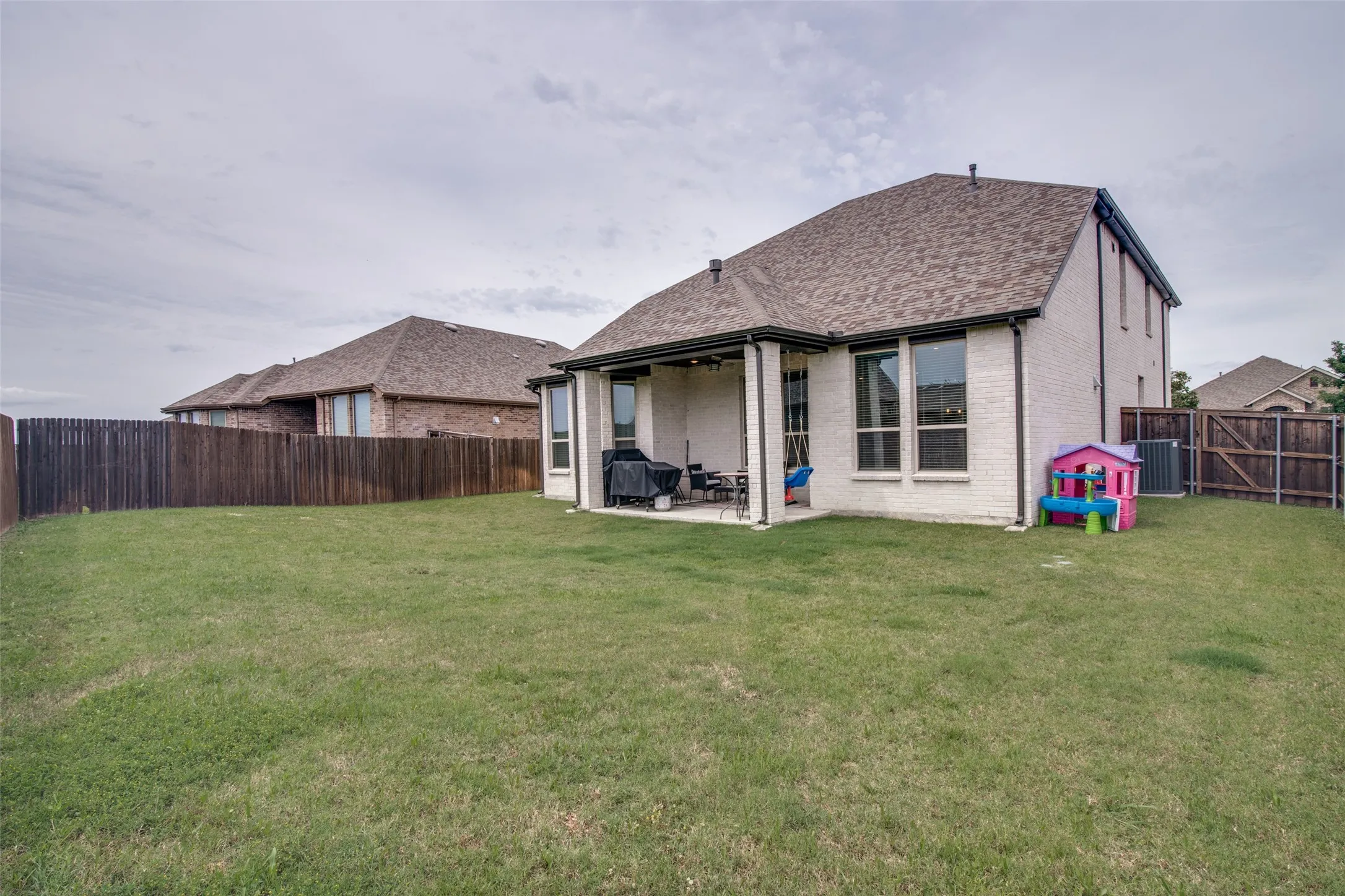 Expansive backyard featuring a manicured lawn, full privacy fencing, and a covered patio