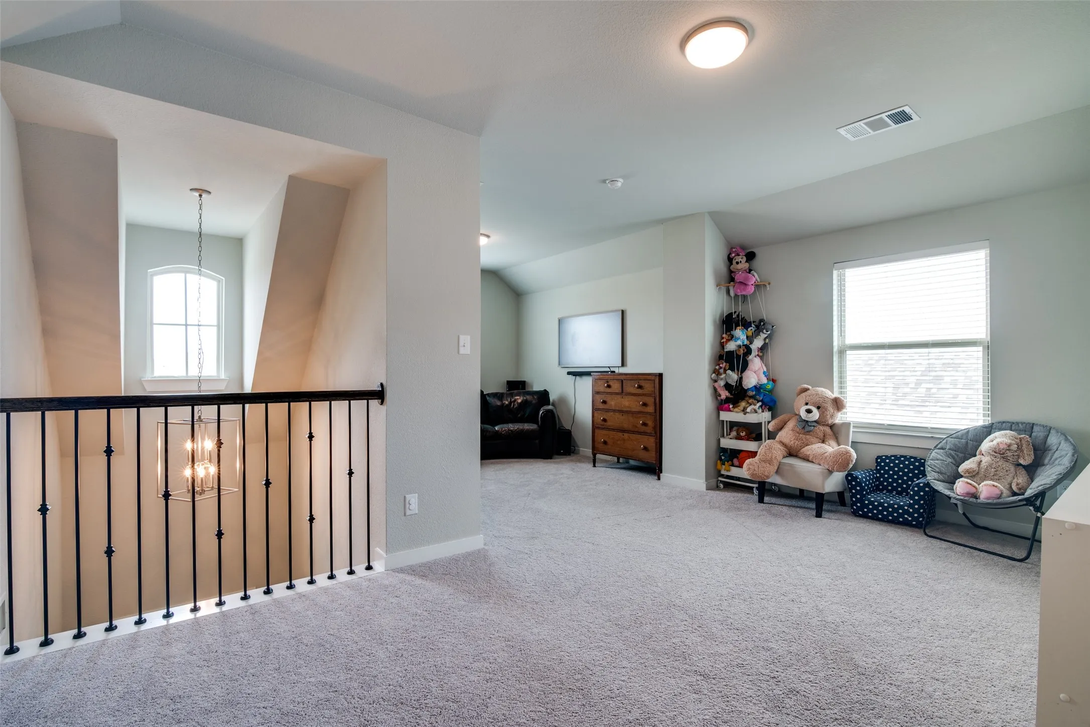 Spacious upstairs landing with light grey carpeting, recessed lighting, a window with blinds, and a black wrought iron stair railing