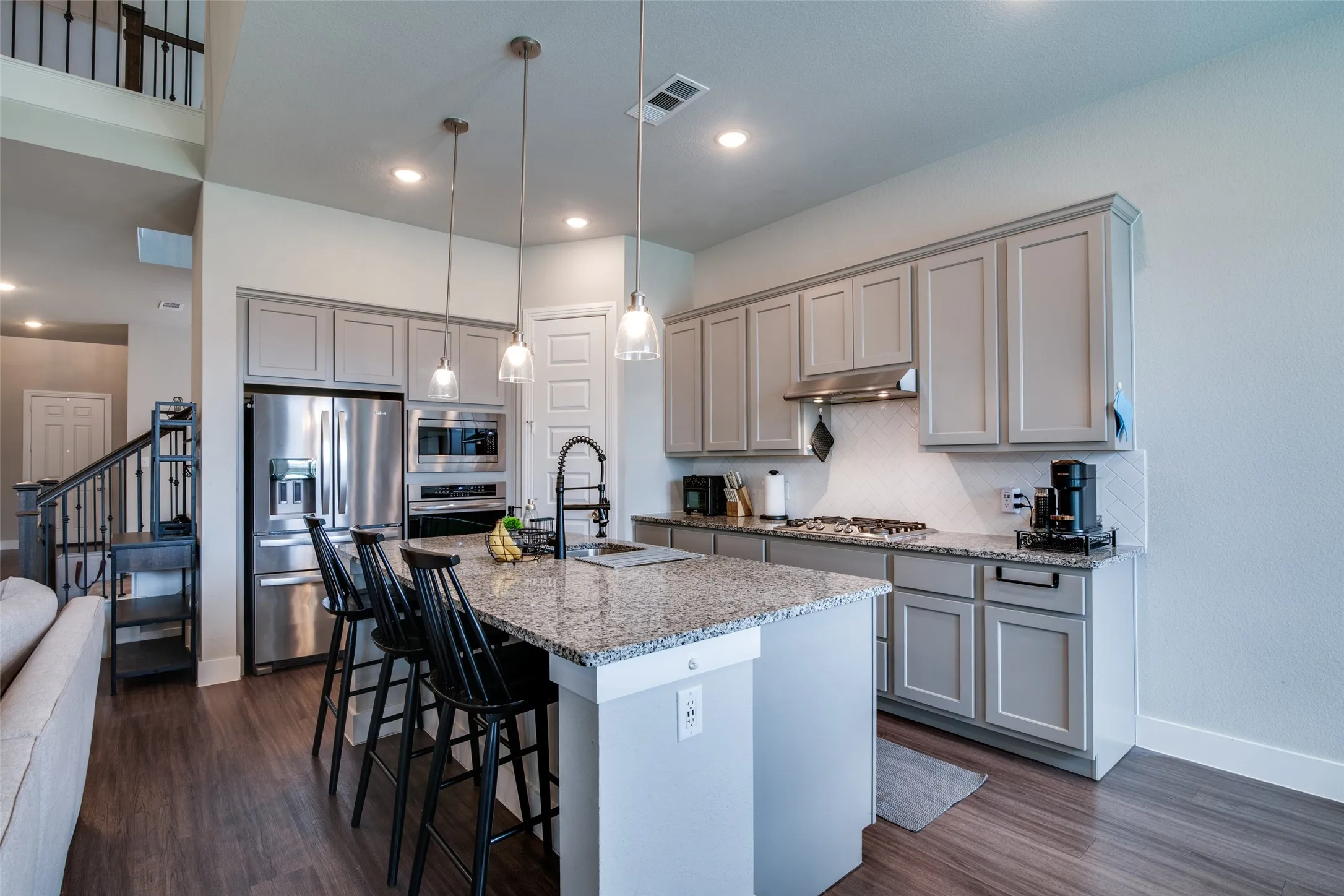 Modern kitchen featuring an expansive island with a stone countertop, pendant lighting, stainless steel appliances, and wood-finish flooring