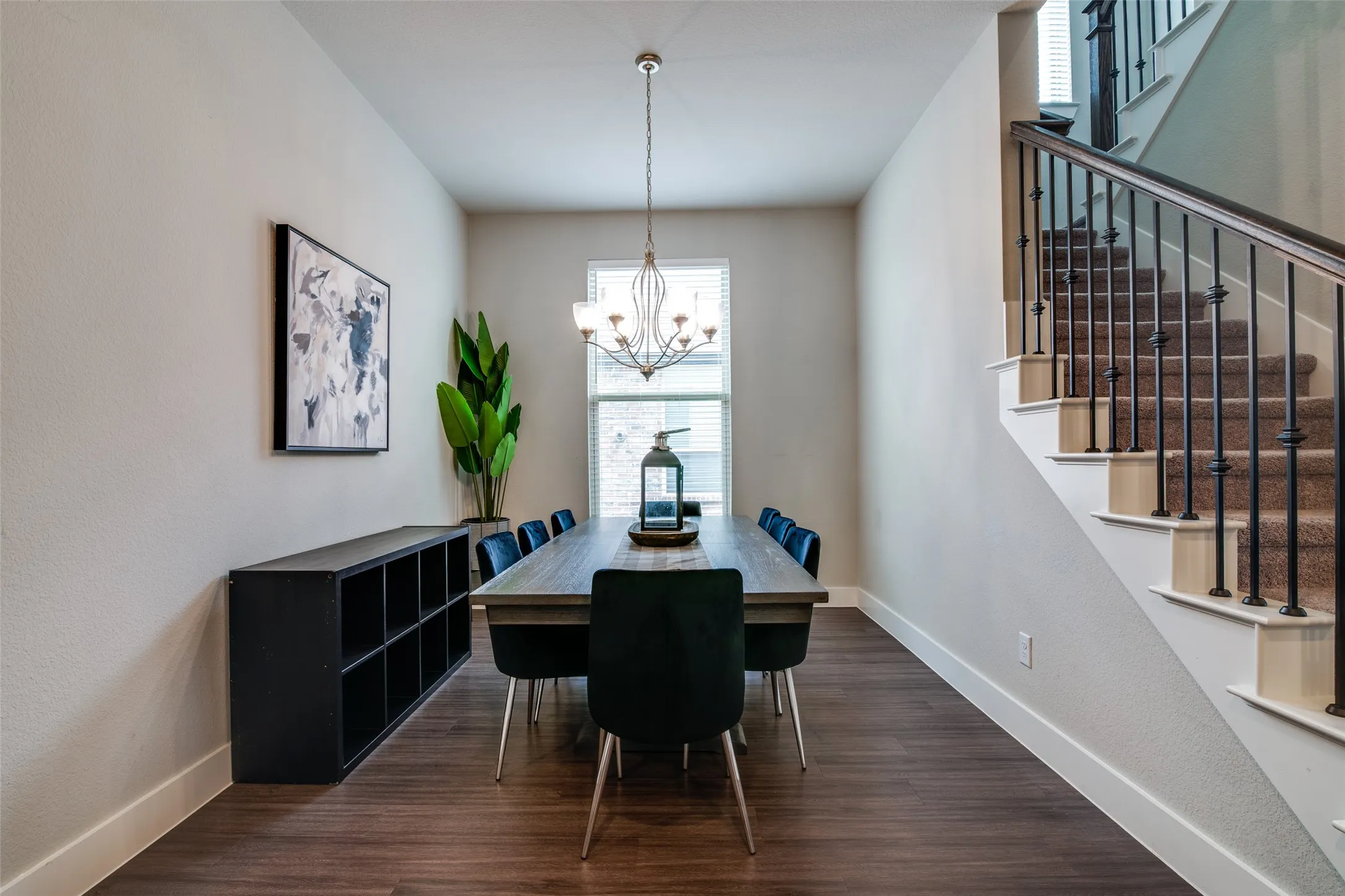 Spacious room featuring wood-finish flooring, a contemporary chandelier, and a large window with privacy blinds