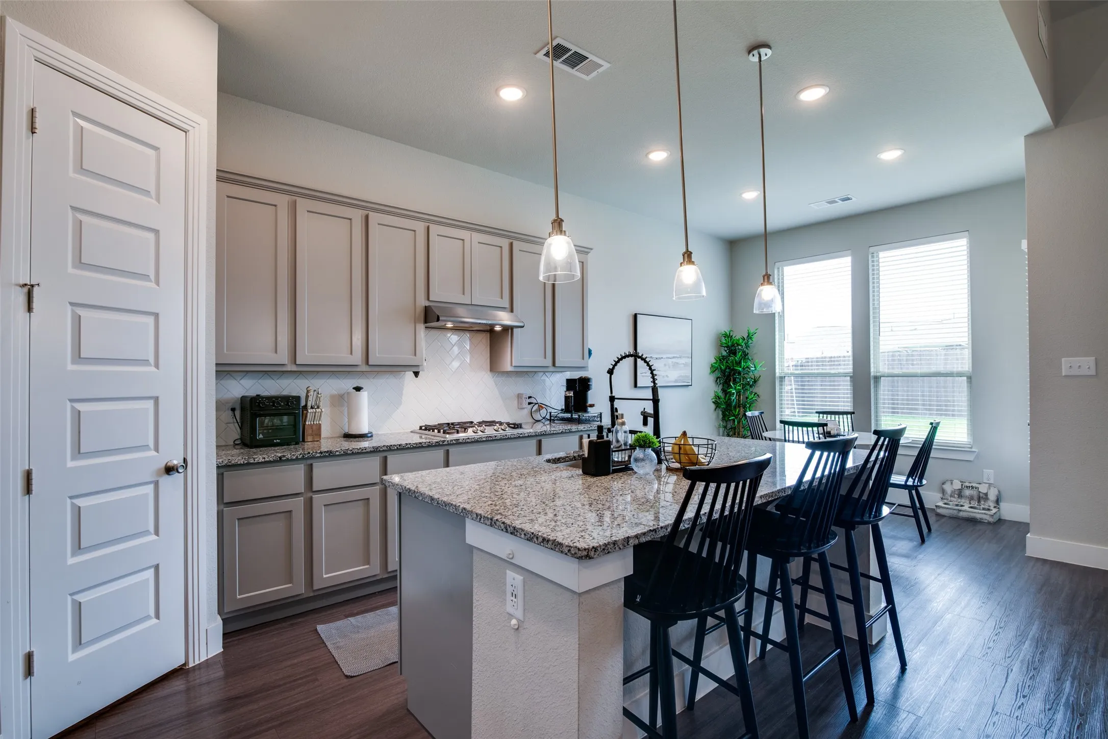Spacious kitchen featuring an expansive island with granite countertops, pendant lighting, a tile backsplash, light gray cabinetry, and wood-finish flooring