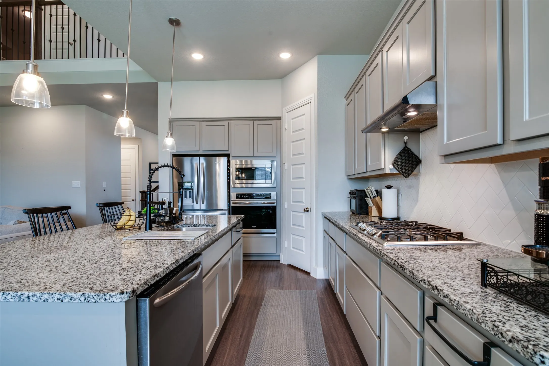 Spacious kitchen featuring an expansive island with a stainless steel sink, pendant lighting, built-in stainless steel appliances, extensive cabinetry, and granite countertops