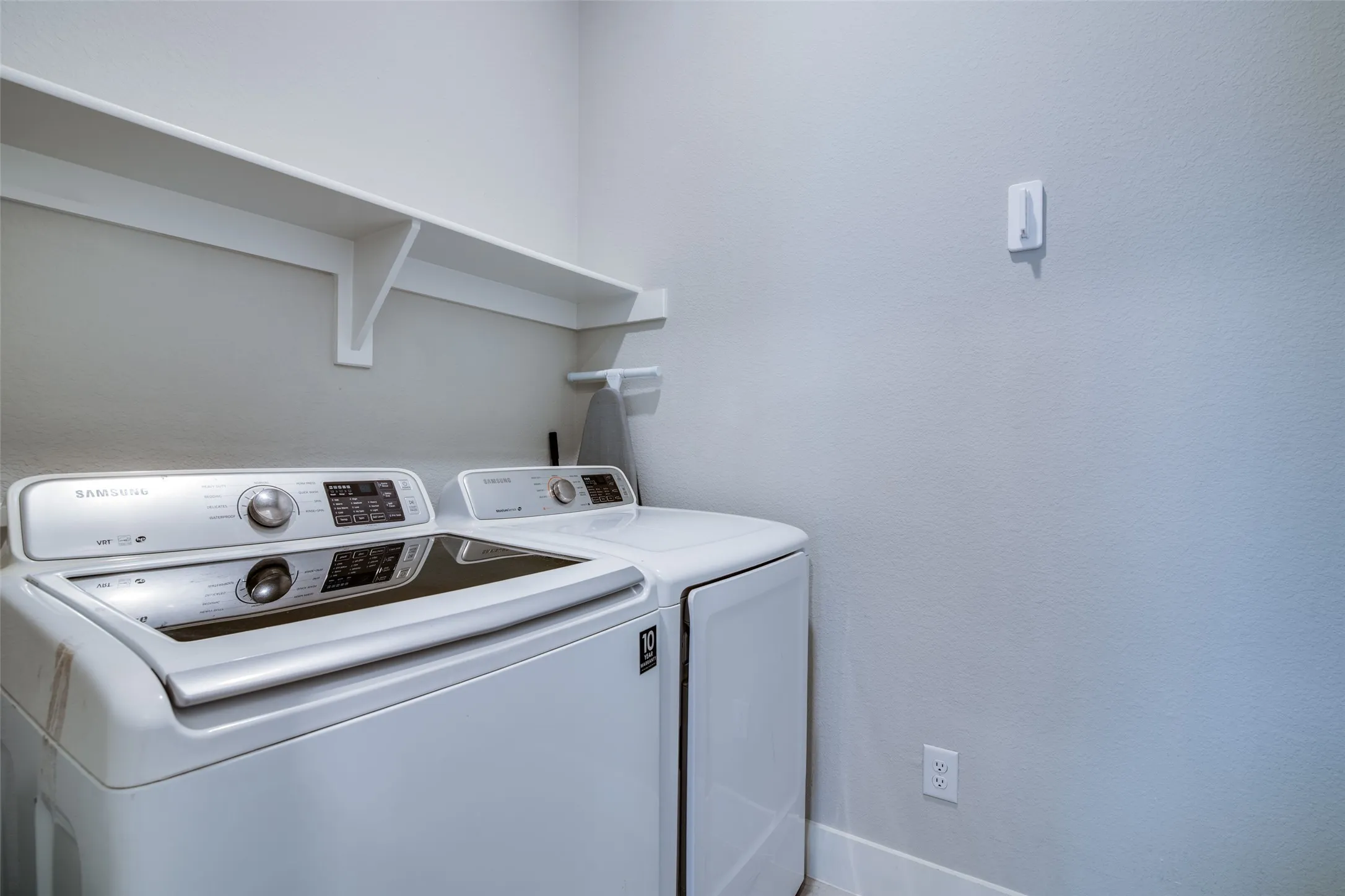 Dedicated laundry area featuring a white washer and dryer, light gray walls, white baseboards, and built-in white shelving