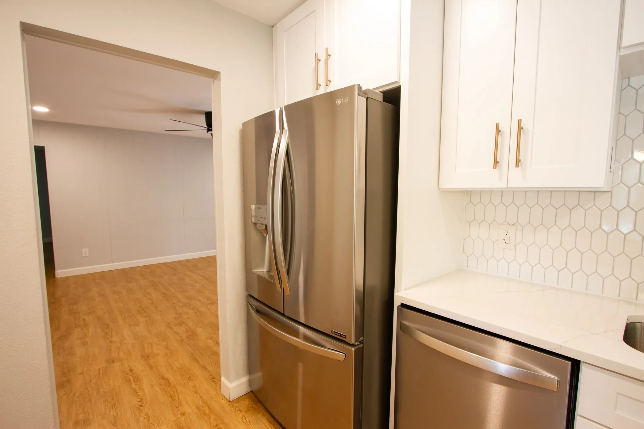 Kitchen featuring appliances with stainless steel finishes, light wood-style floors, backsplash, white cabinets, and light stone counters