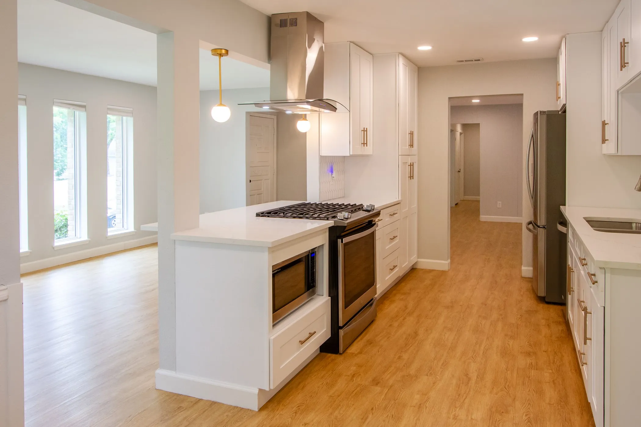 Kitchen with exhaust hood, stainless steel appliances, white cabinets, light countertops, and light wood-type flooring