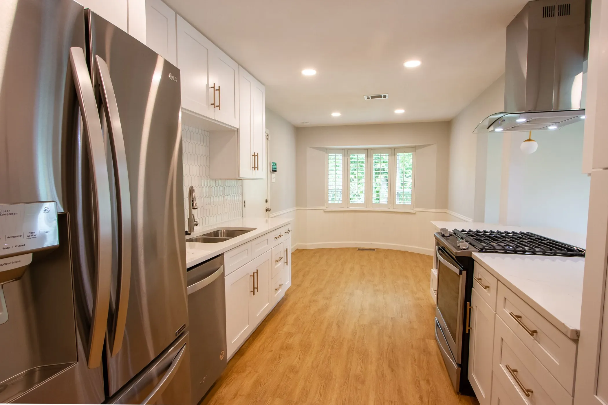 Kitchen featuring stainless steel appliances, wall chimney range hood, a sink, light wood-type flooring, and white cabinets