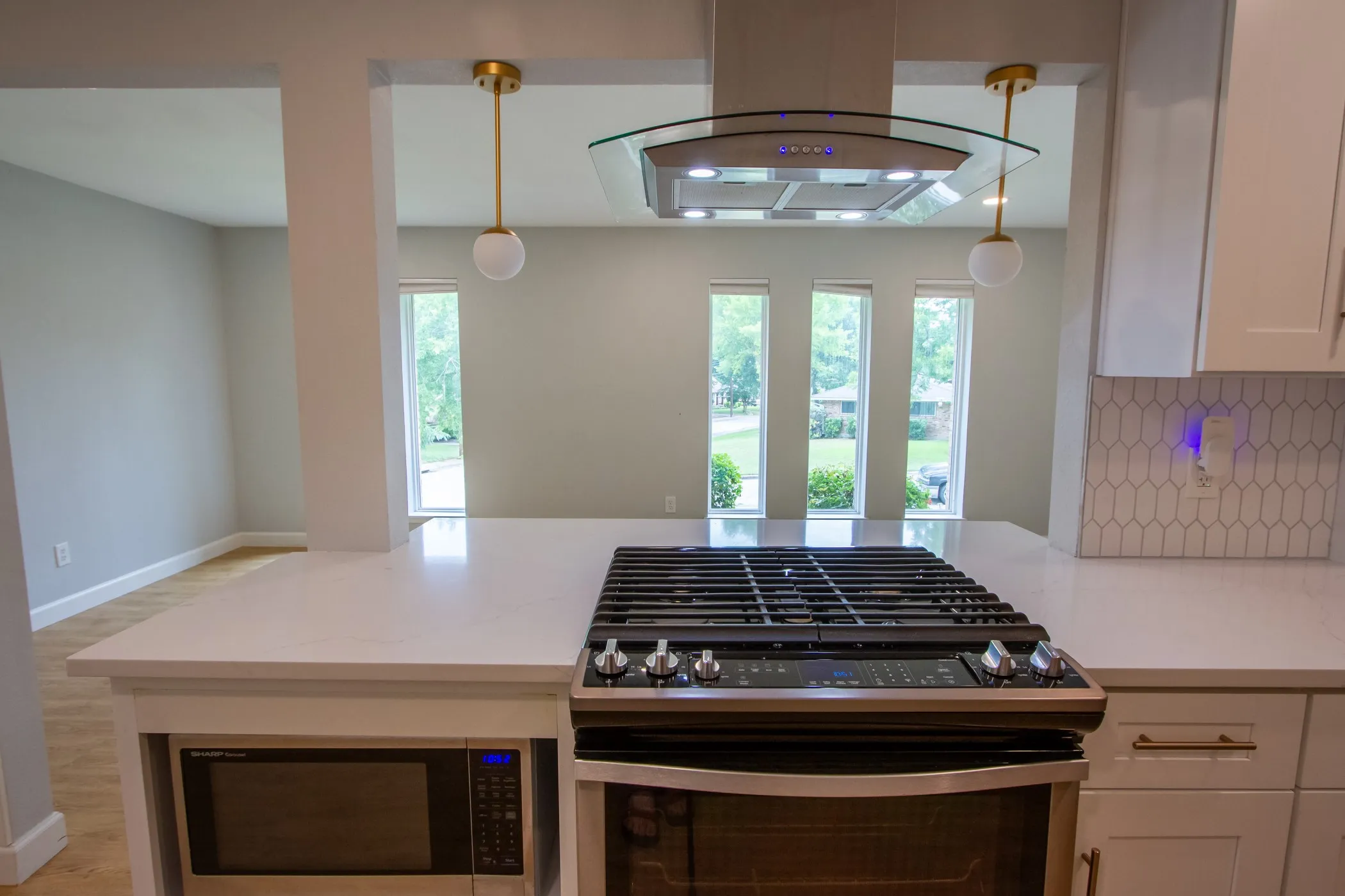 Kitchen featuring gas stove, island range hood, stainless steel microwave, white cabinetry, and pendant lighting