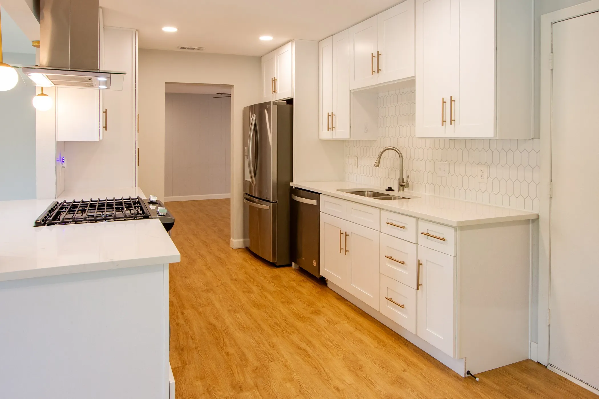 Kitchen with island range hood, appliances with stainless steel finishes, a sink, tasteful backsplash, and light wood-type flooring