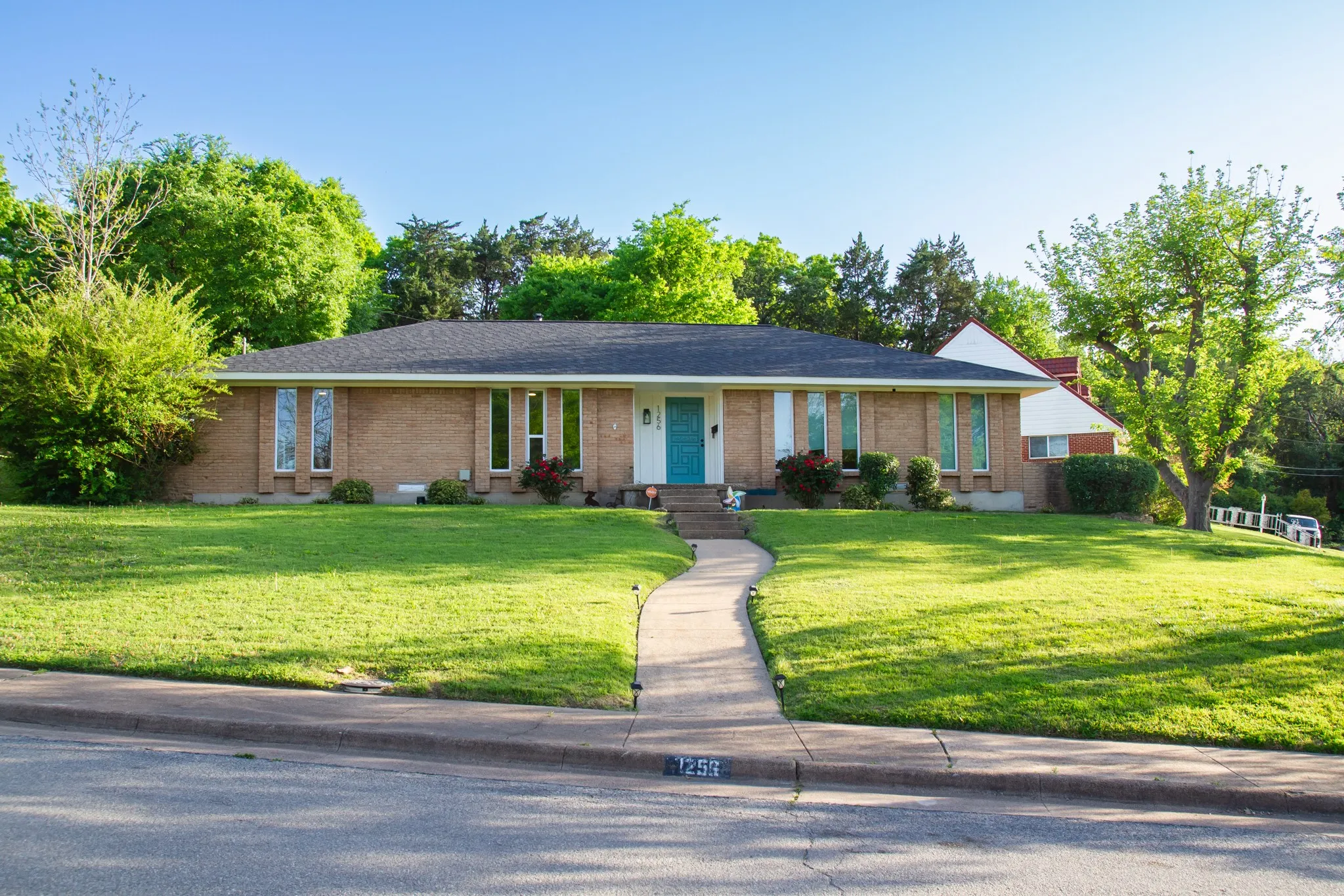 Ranch-style home with roof with shingles, brick siding, and a front lawn