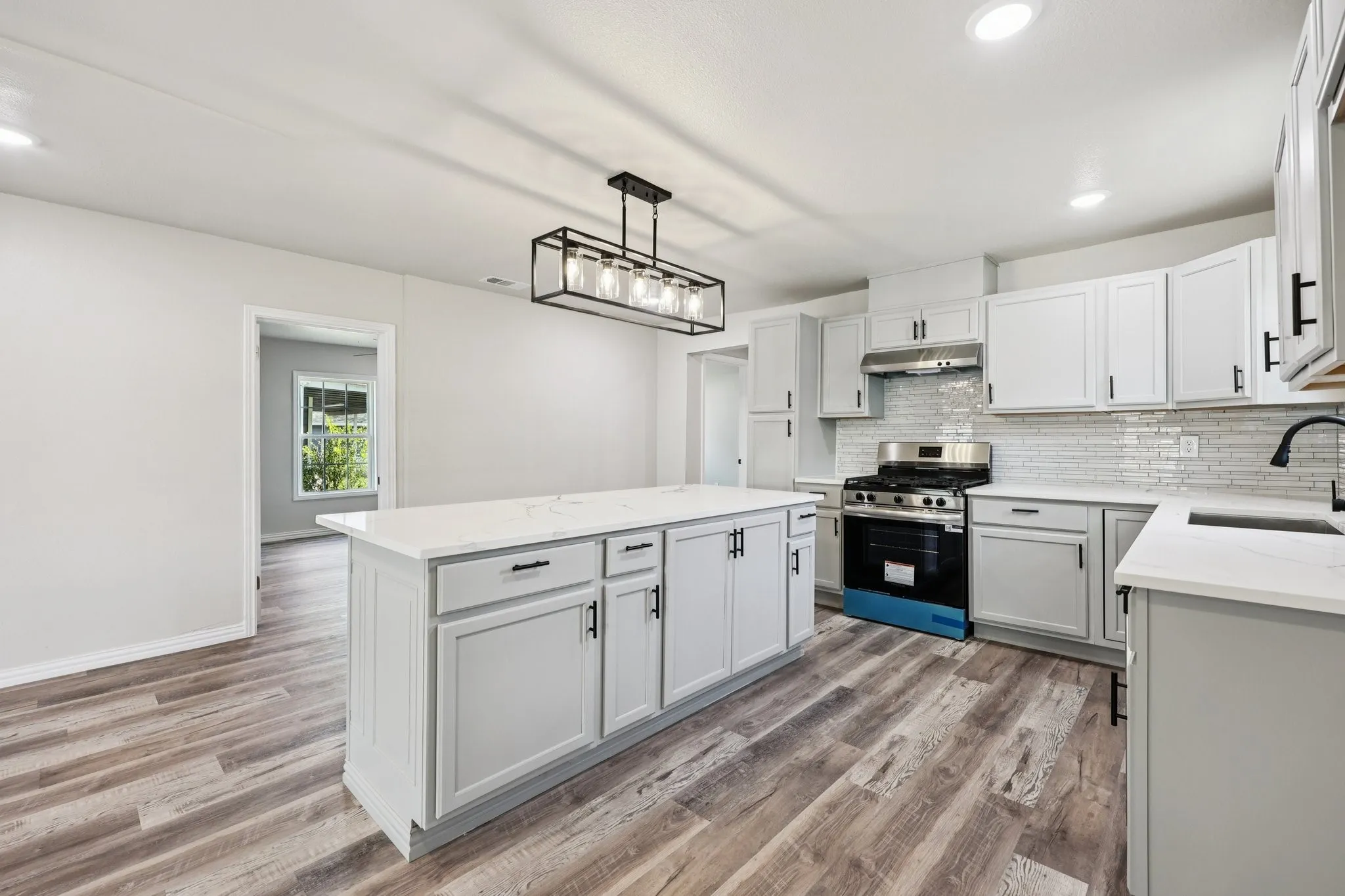 Contemporary kitchen featuring a spacious island with a white countertop, light gray cabinetry, wood-finish flooring, a stainless steel range, and a subway tile backsplash