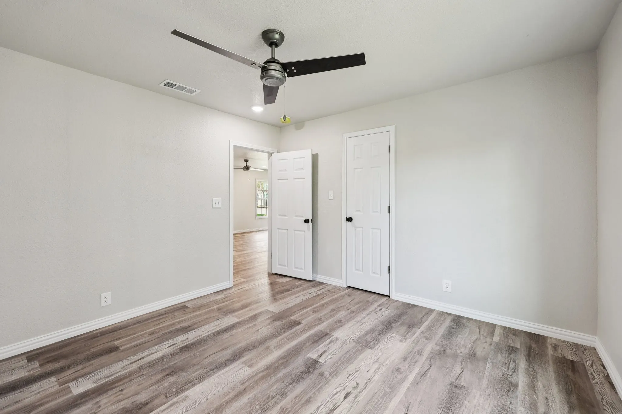 Spacious room featuring wood-finish flooring, light neutral wall tones, and a modern ceiling fan