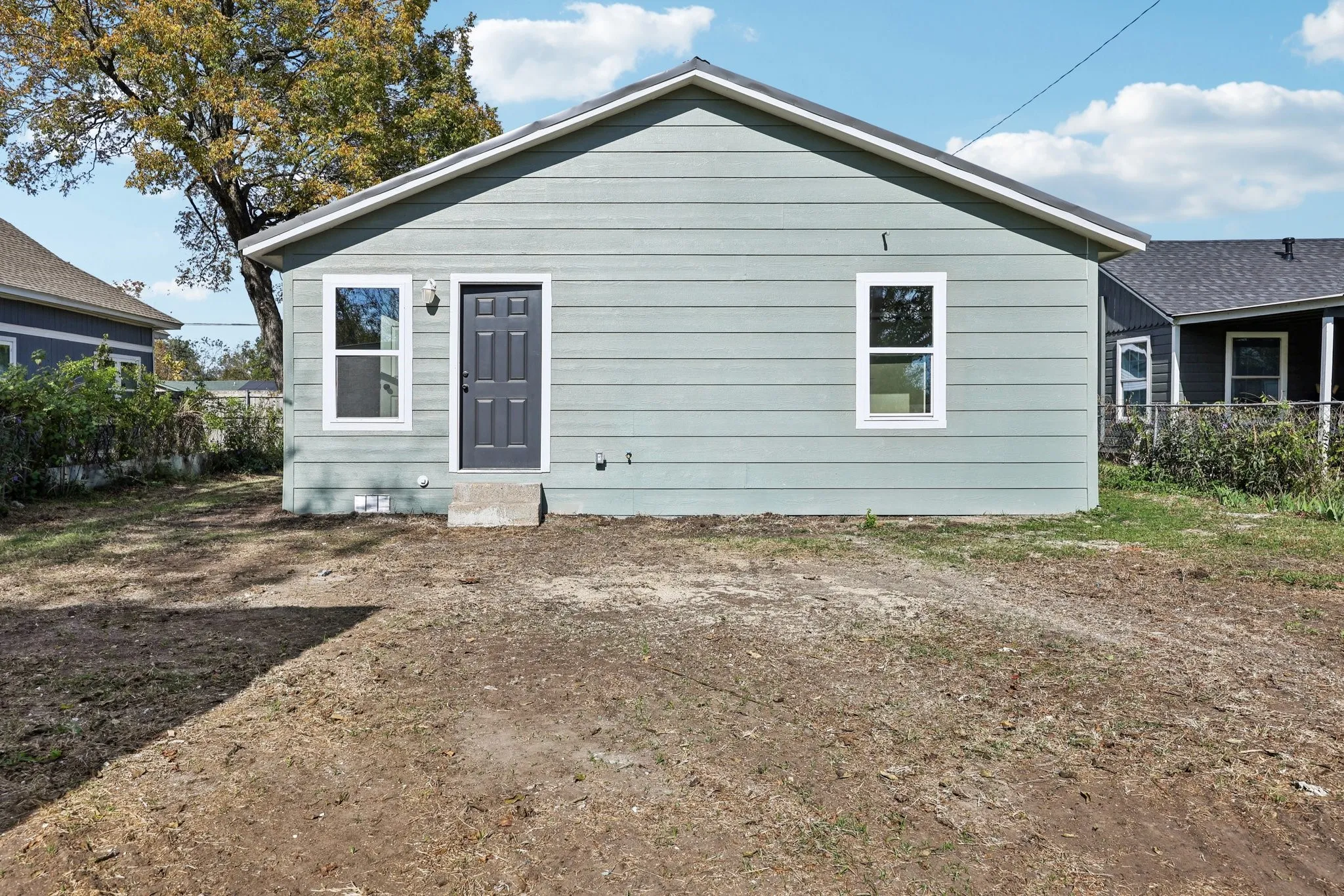 Rear exterior featuring light green siding, two white-framed windows, and a dark gray entry door
