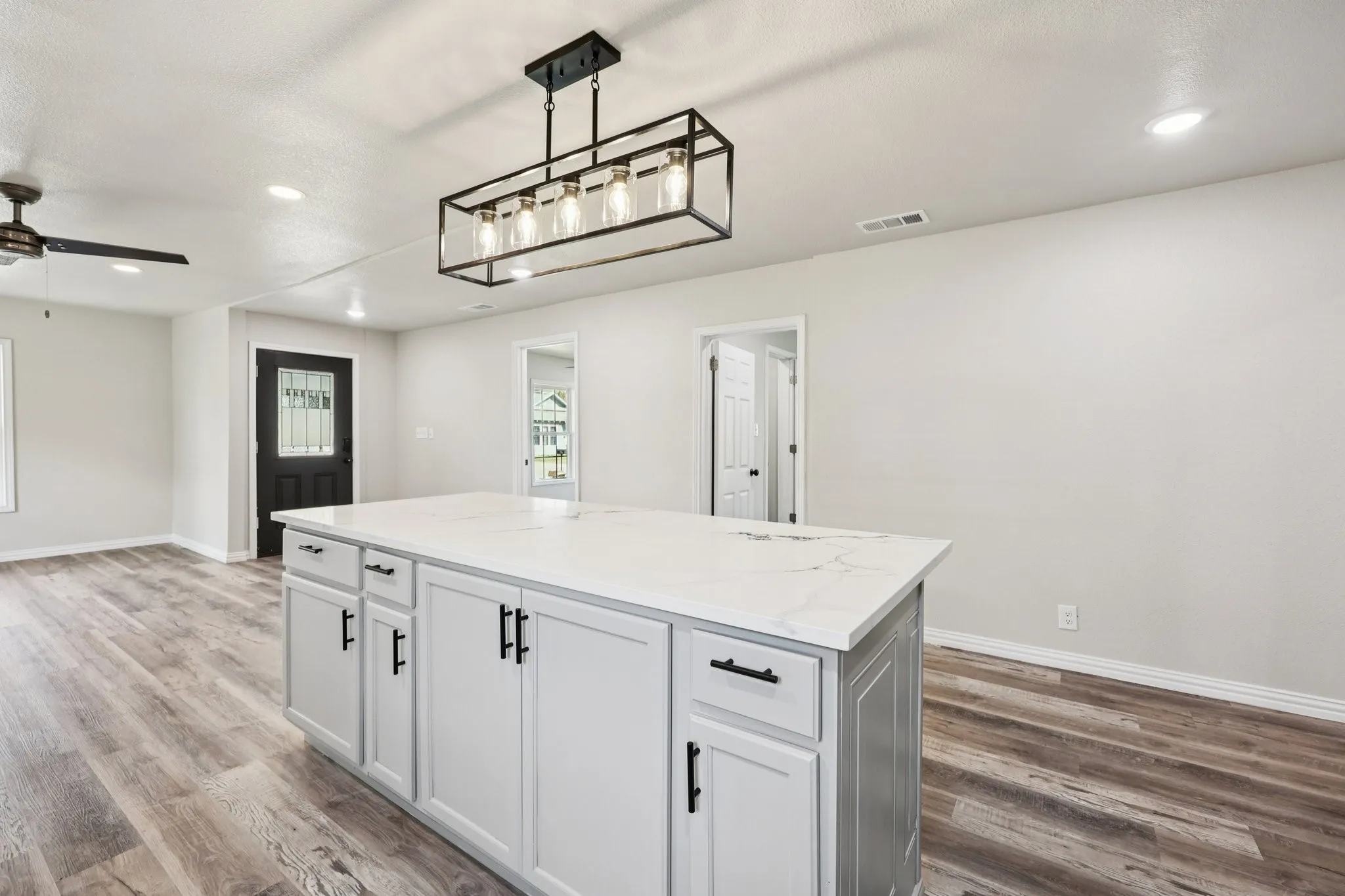 Kitchen island featuring a light-toned countertop, light grey cabinetry with black hardware, and an overhead rectangular chandelier