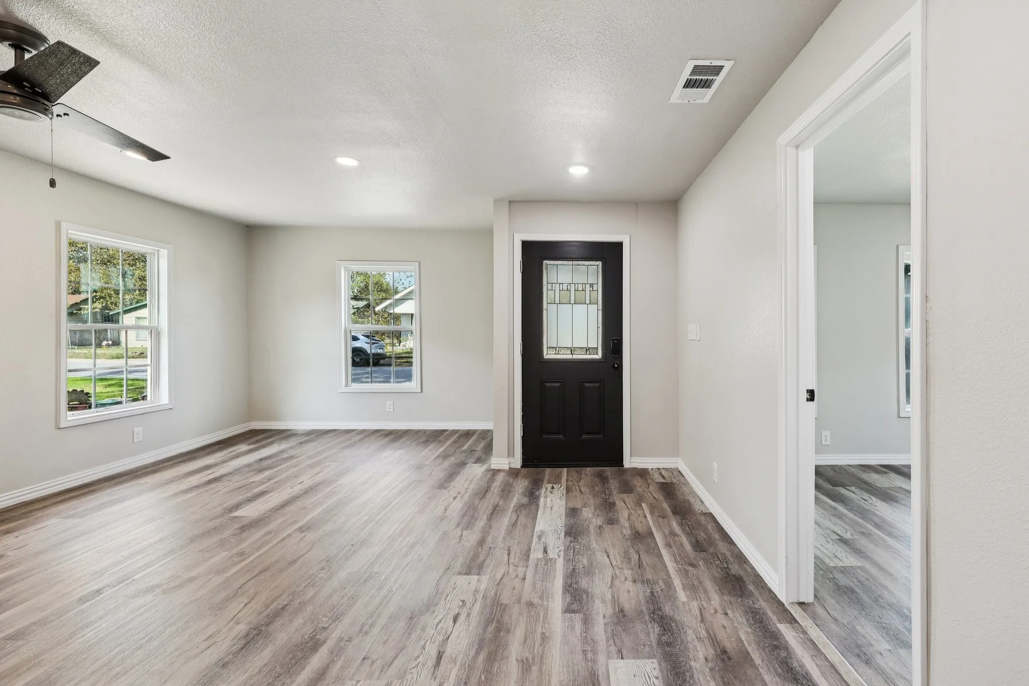 Spacious room featuring wood-finish flooring, two large windows, a ceiling fan, and recessed lighting
