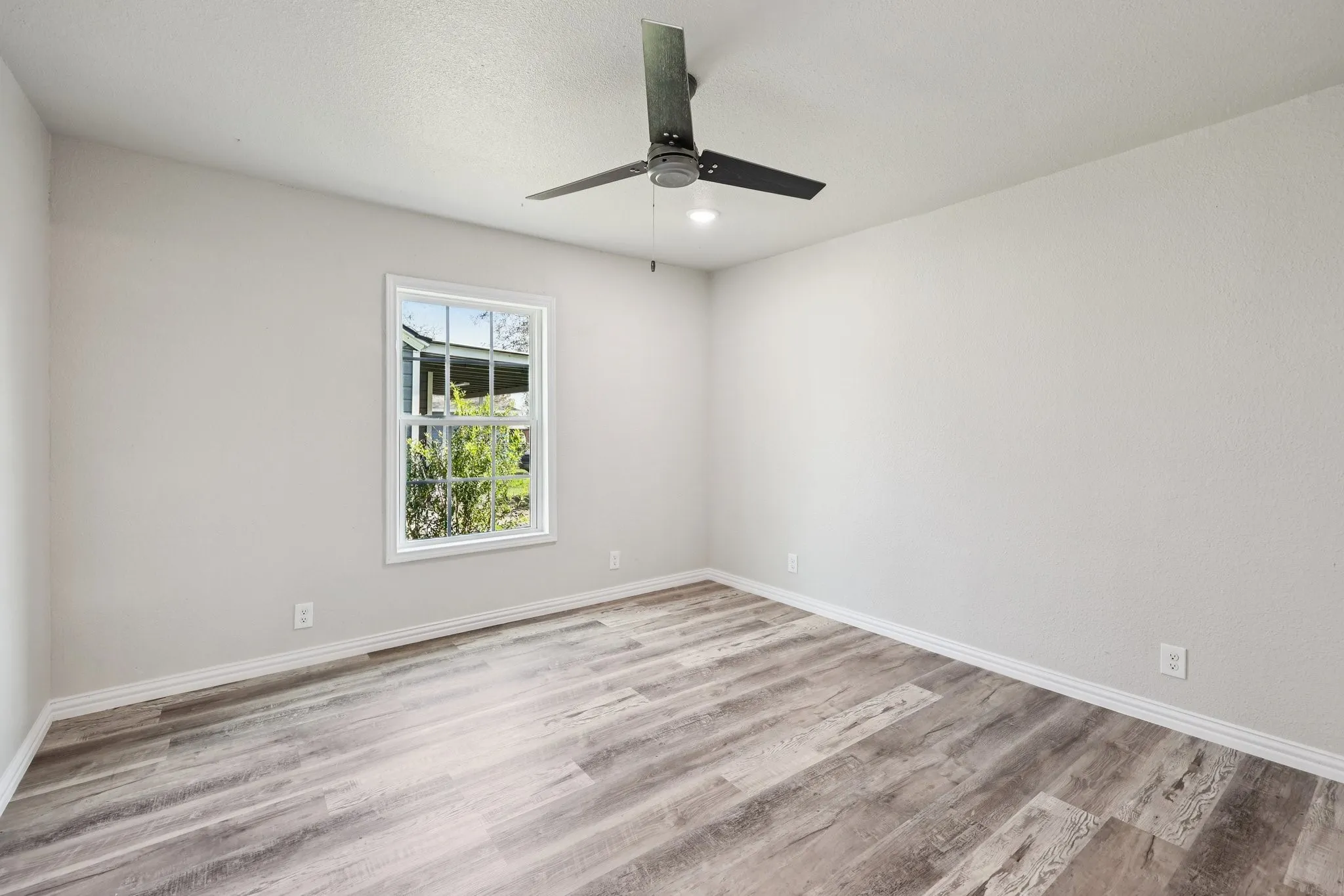 Room featuring wood-finish flooring, white baseboards, a white window frame, and a ceiling fan with integrated lighting