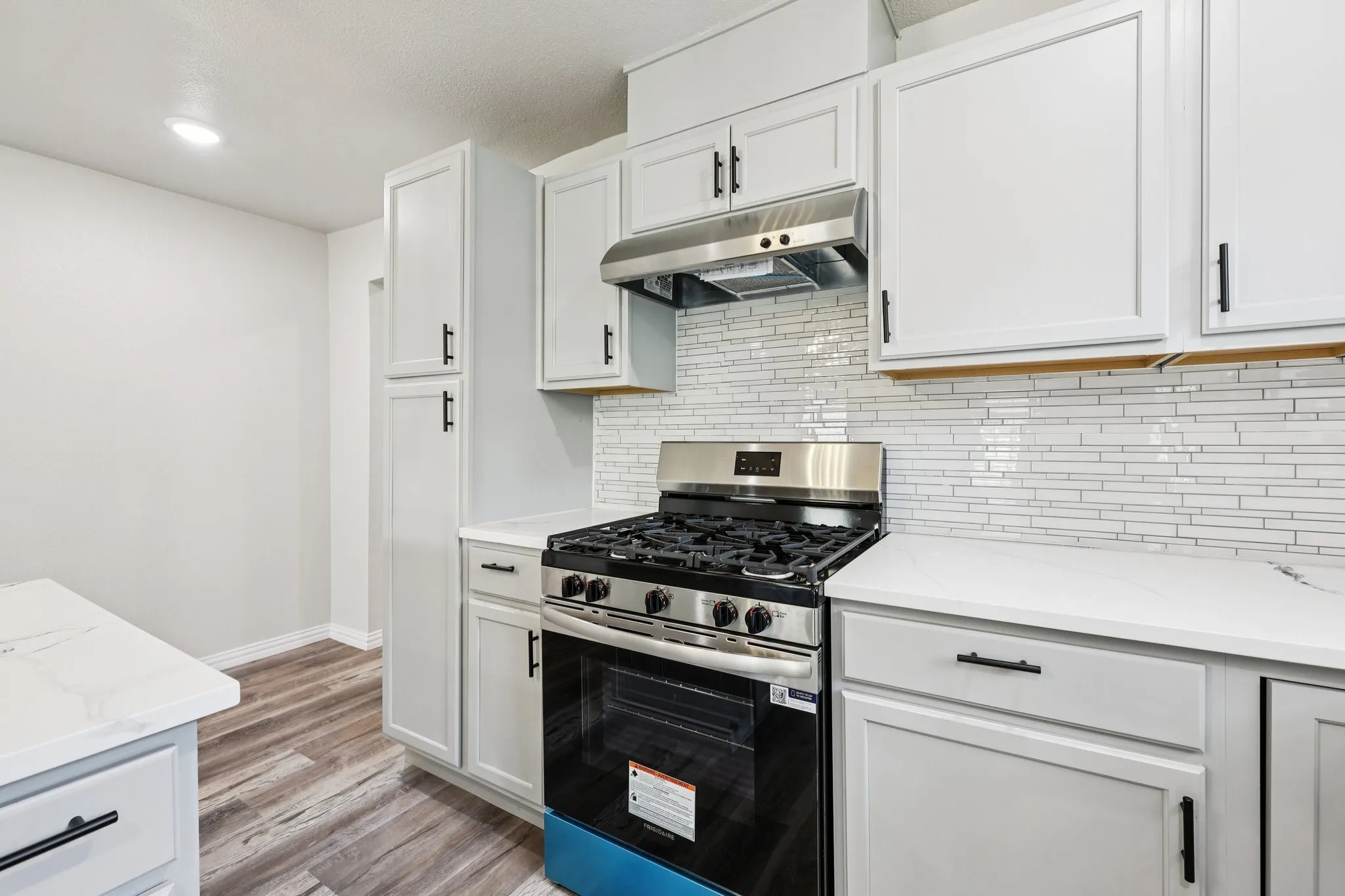 Modern kitchen featuring light gray cabinetry with black hardware, white countertops, stainless steel range, and a full-height stacked tile backsplash