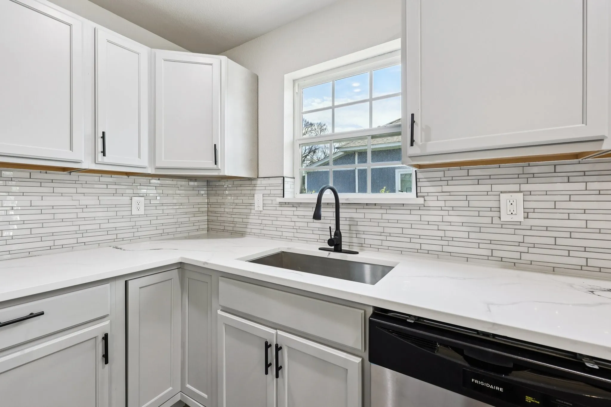 Corner kitchen sink area featuring white shaker-style cabinetry, a white quartz countertop, and a contemporary tile backsplash