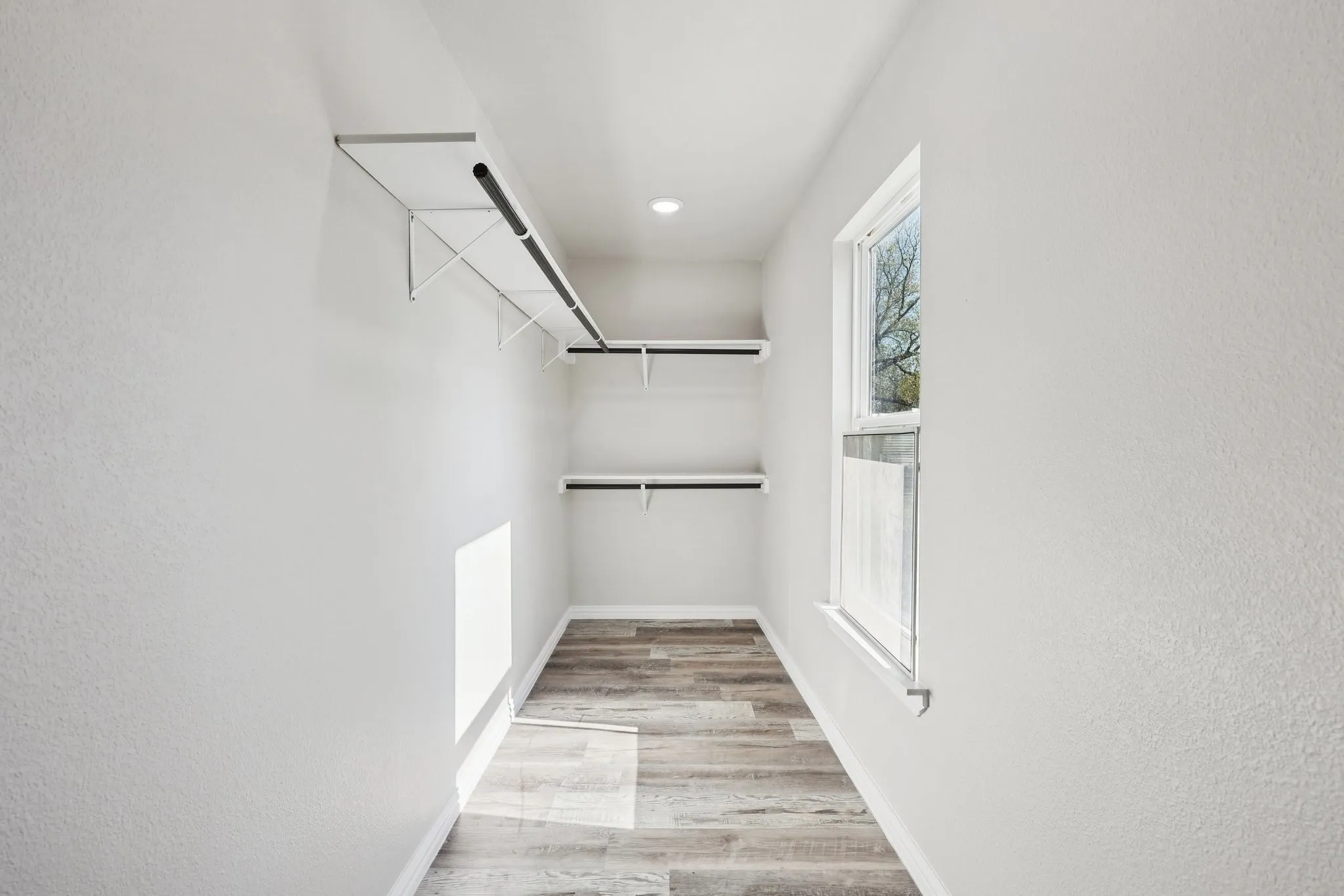 Walk-in closet featuring wood-finish flooring, a window, recessed lighting, and white shelving with hanging rods