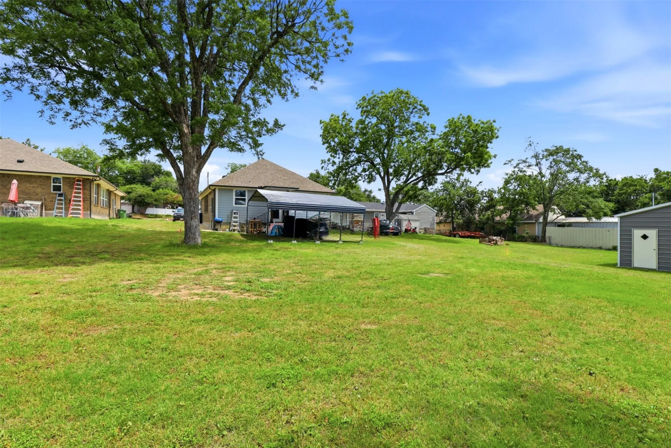 Expansive green lawn with mature trees and a detached storage shed