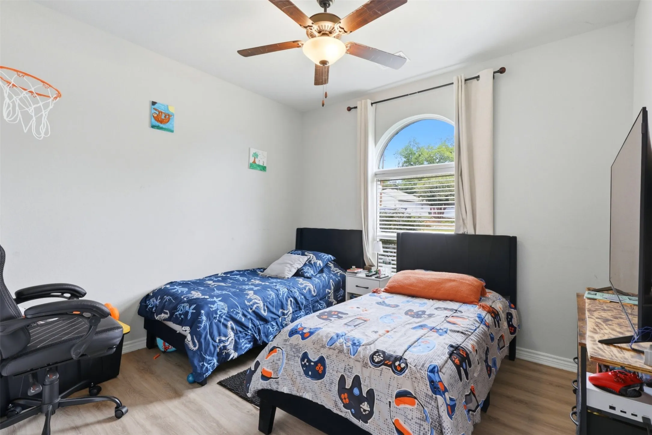 Bedroom featuring light-tone wood-finish flooring, a ceiling fan with light fixture, and a large arched window with blinds