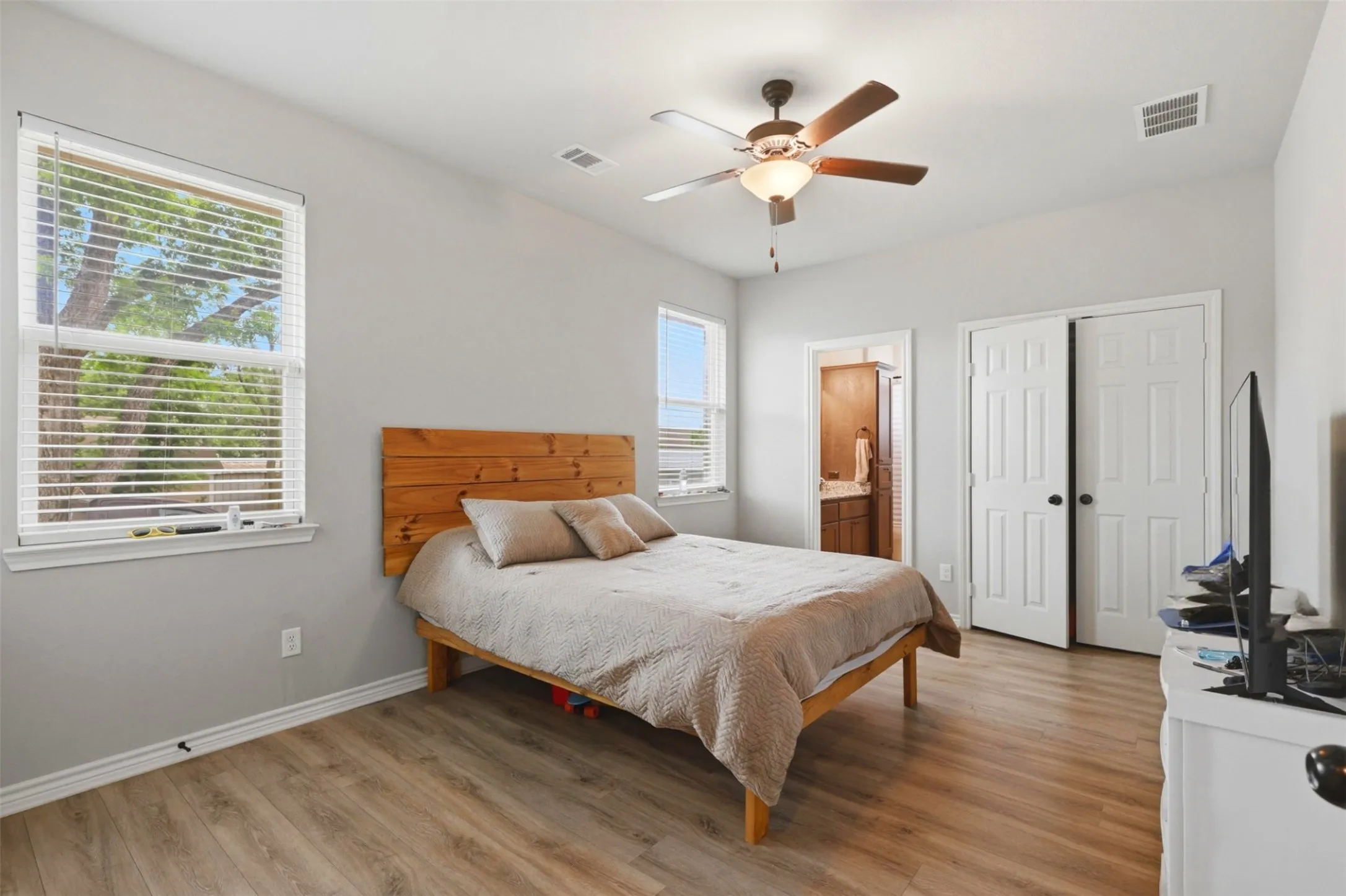 Bedroom featuring wood-finish flooring, two large windows with blinds, a ceiling fan with integrated lighting, and white bi-fold closet doors