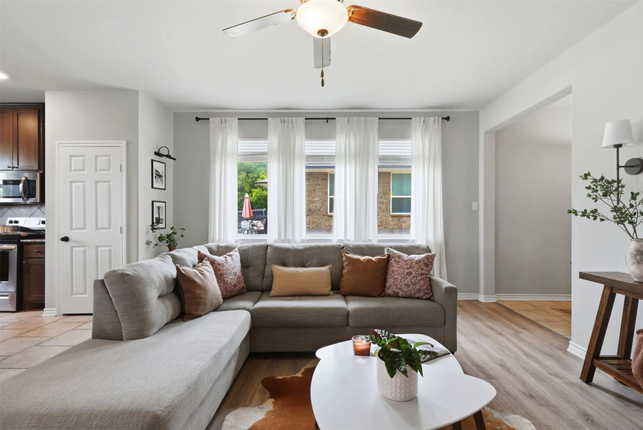 Living area featuring light wood-finish flooring, white walls, and a ceiling fan with integrated lighting