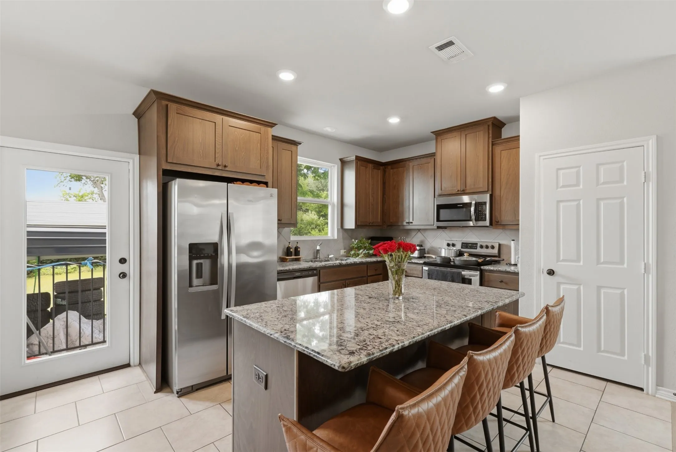 Kitchen featuring a central island with a granite countertop, stainless steel appliances, wood cabinetry, recessed lighting, and tile flooring