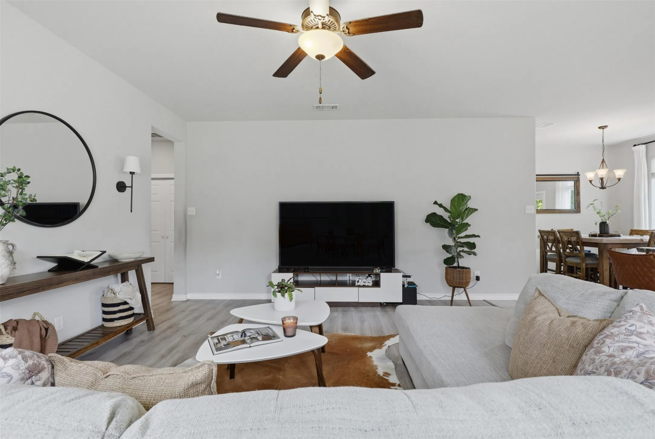 Spacious living area featuring light gray walls, wood-finish flooring, and a ceiling fan with integrated lighting