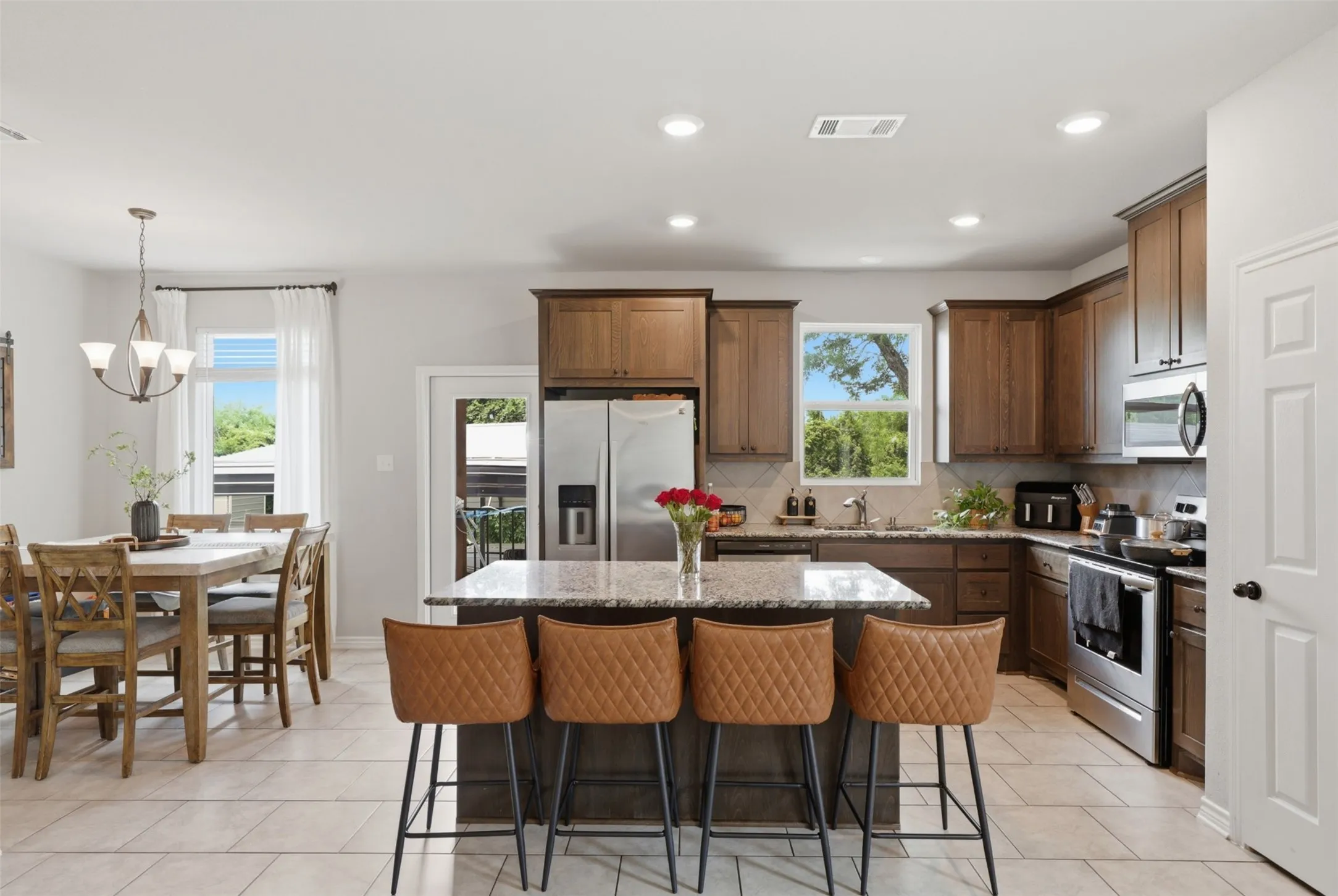 Kitchen featuring an island with stone countertop, stainless steel appliances, wood-finish cabinetry, and tiled flooring