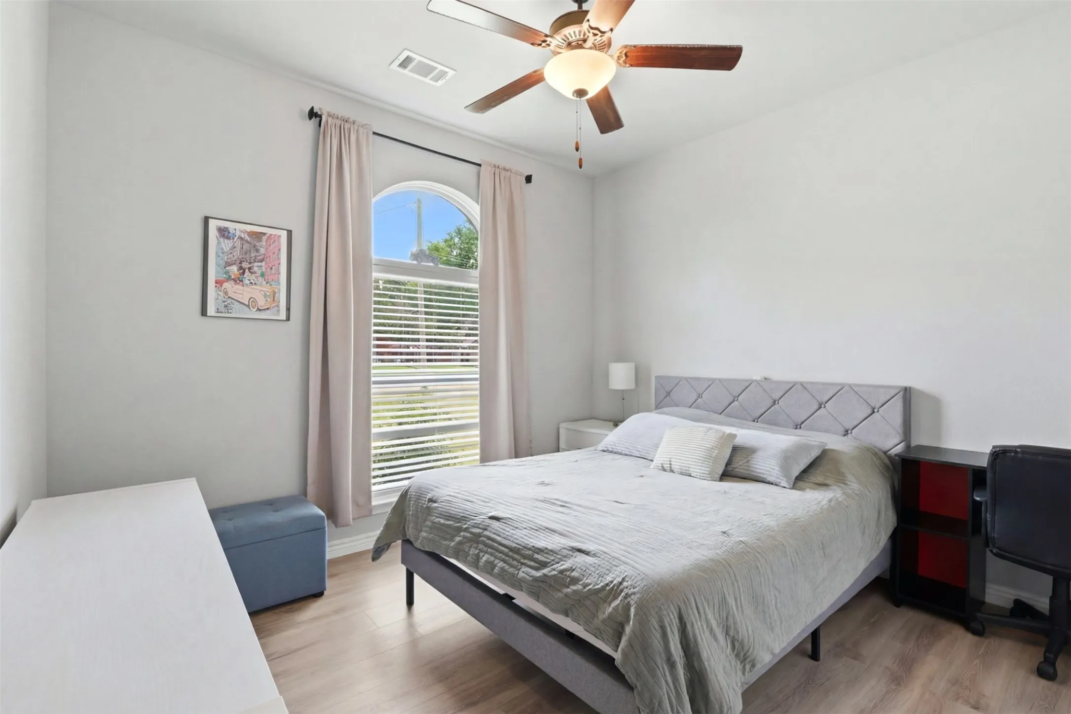 Bedroom featuring a prominent arched window with blinds and drapery