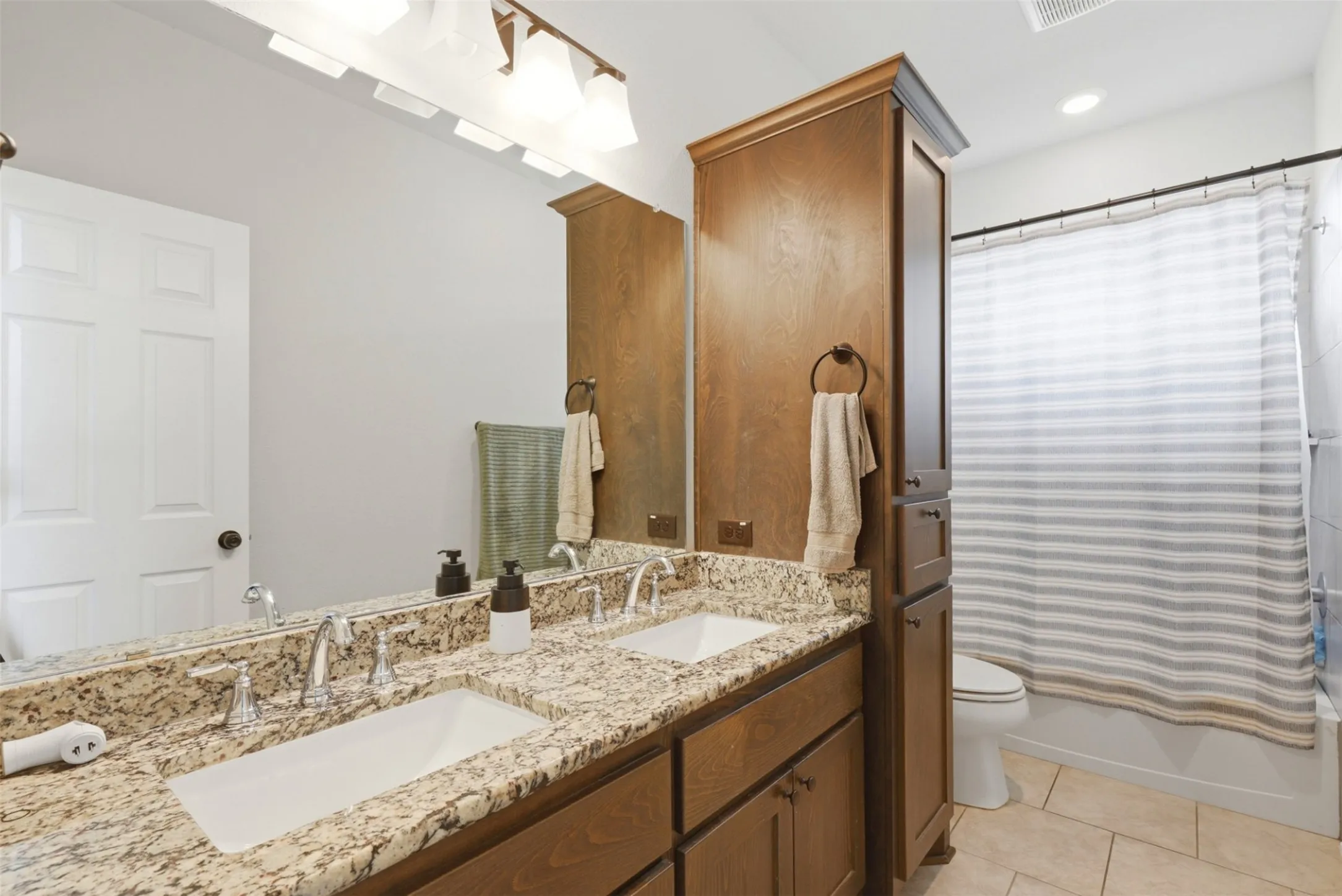 Double vanity featuring stone countertops with integrated sinks, wood cabinetry, and chrome fixtures